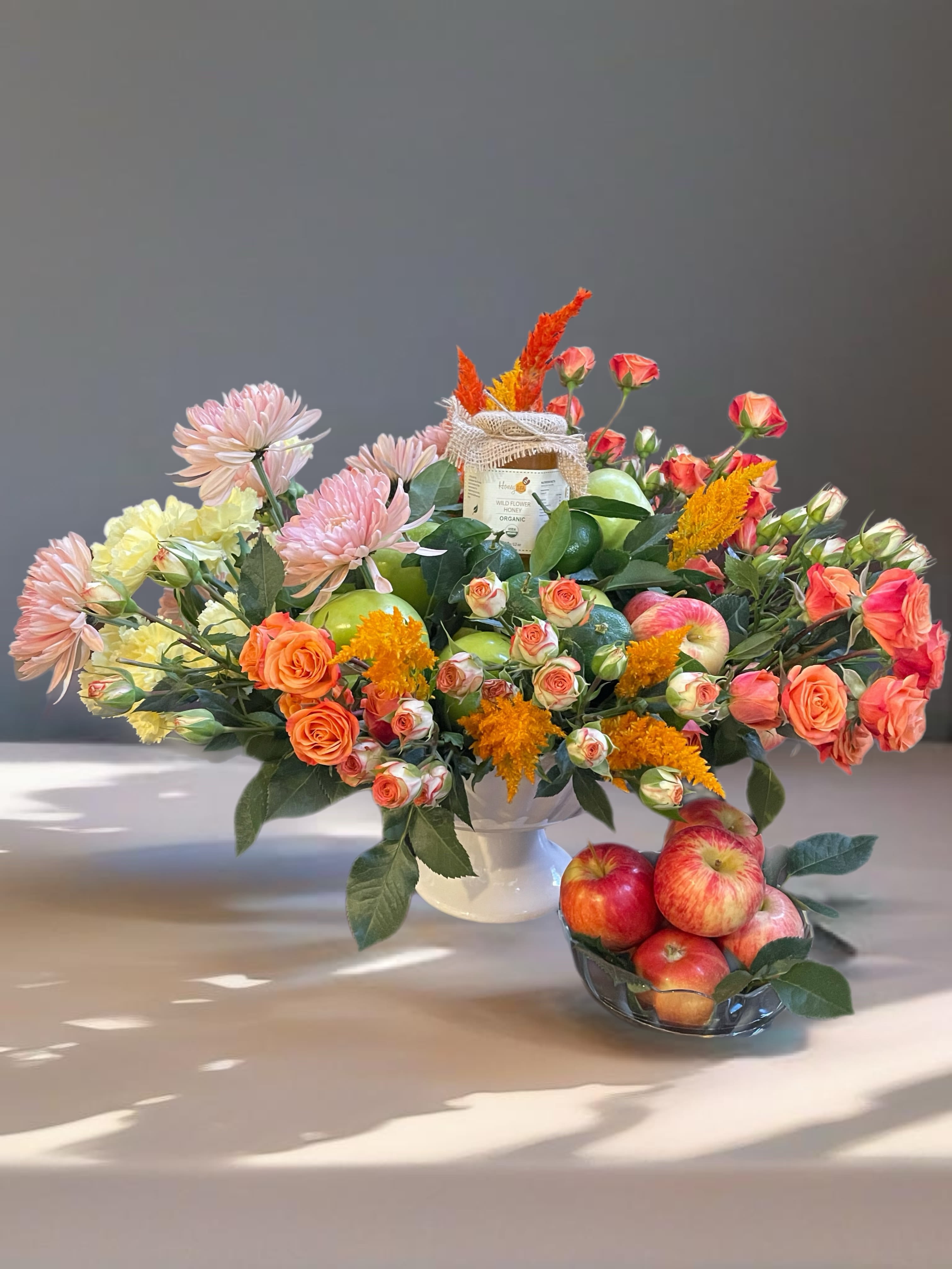 Mixed bouquet in a white vase with apples and a small bowl of apples