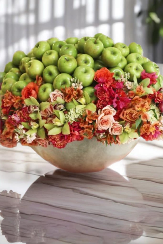 Bowl arrangement topped with green apples and colorful flowers