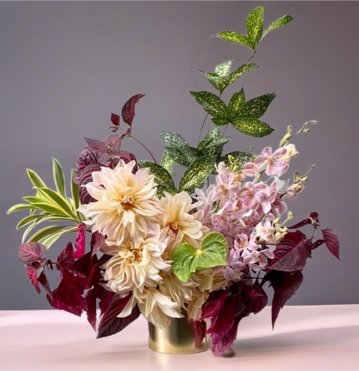 Arrangement of cream dahlias and pink orchids in a gold vase