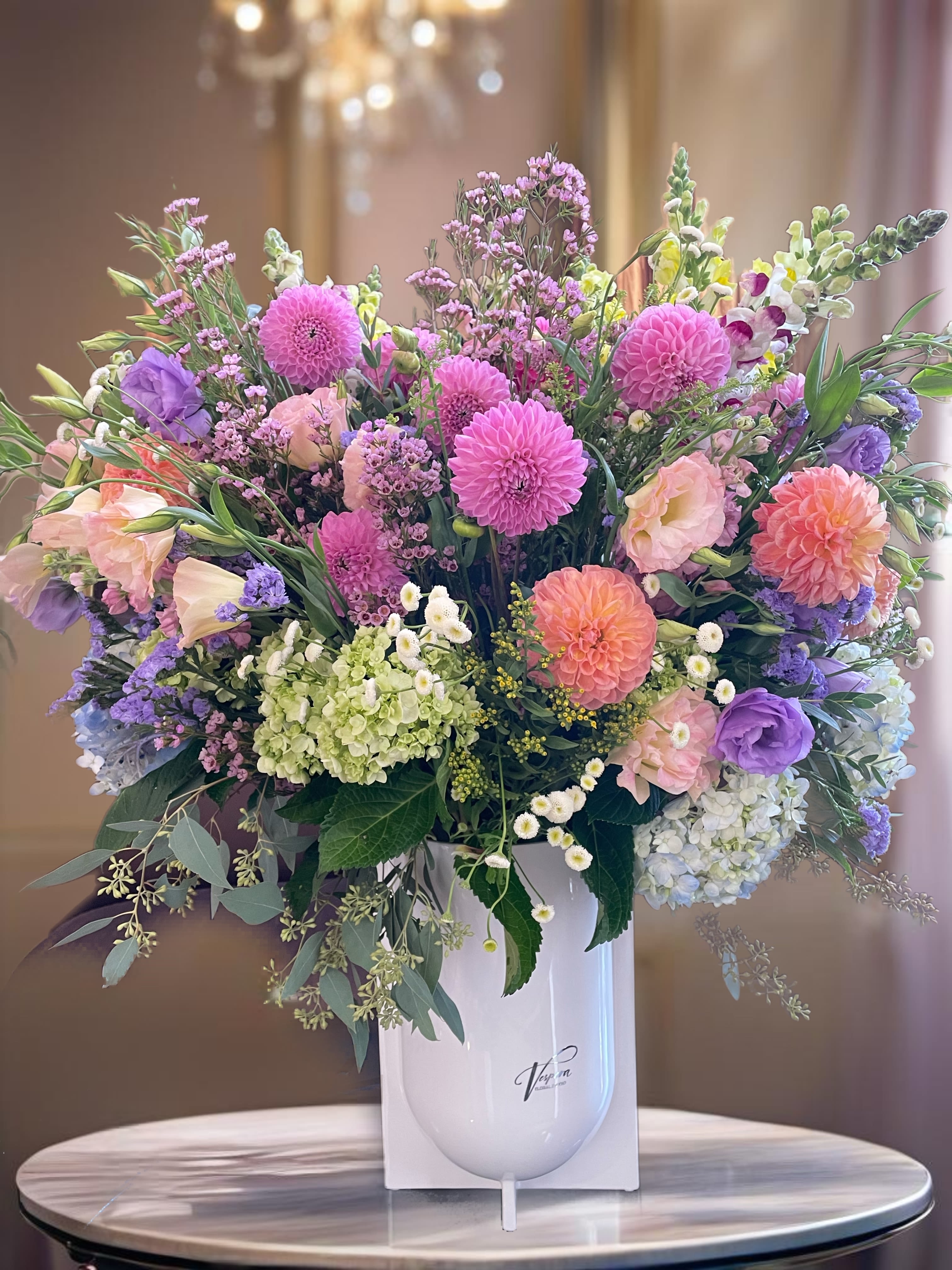 Large pastel bouquet in a white vase with pink, purple, peach, and green blooms