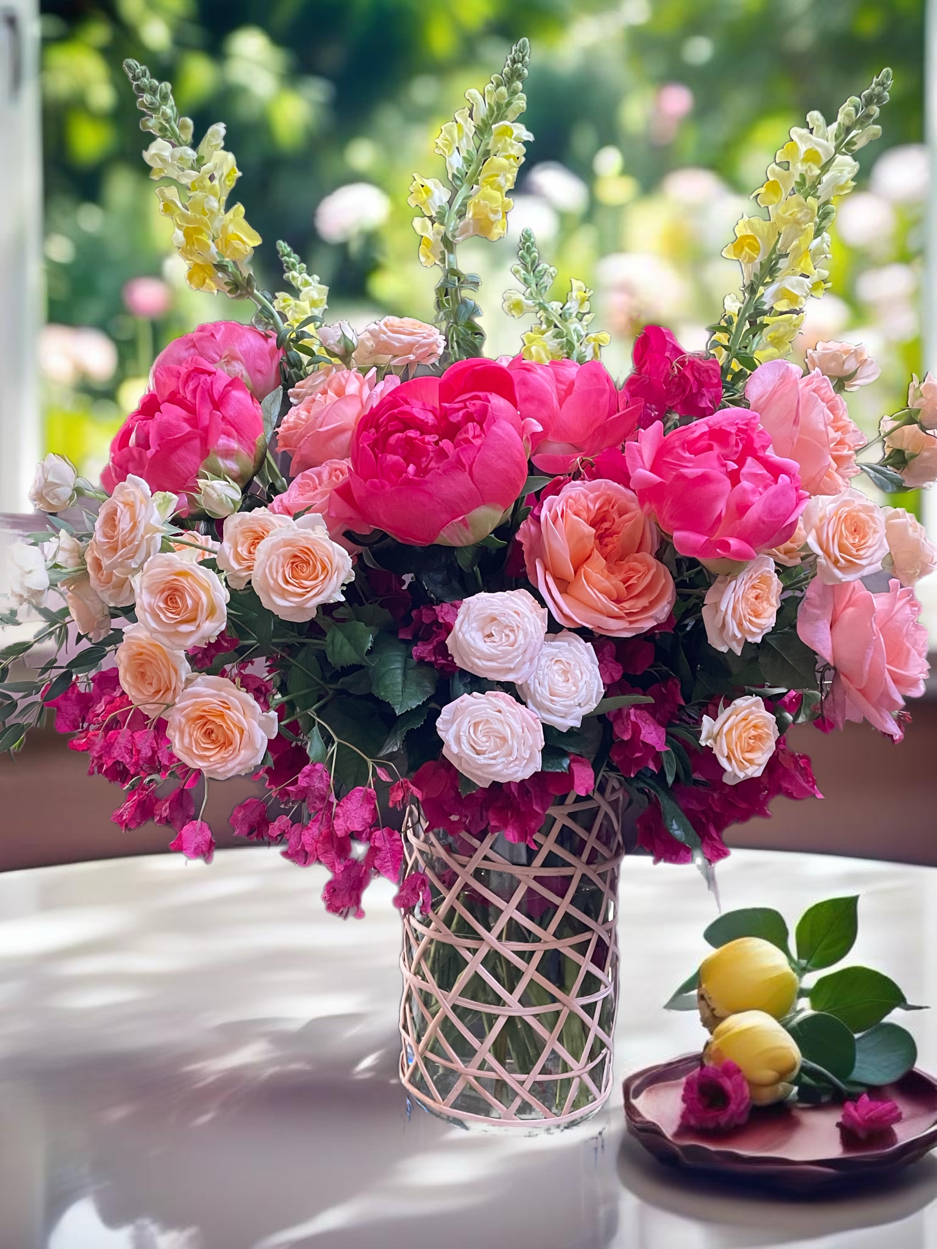 Pink and peach floral arrangement in a glass vase with yellow snapdragons