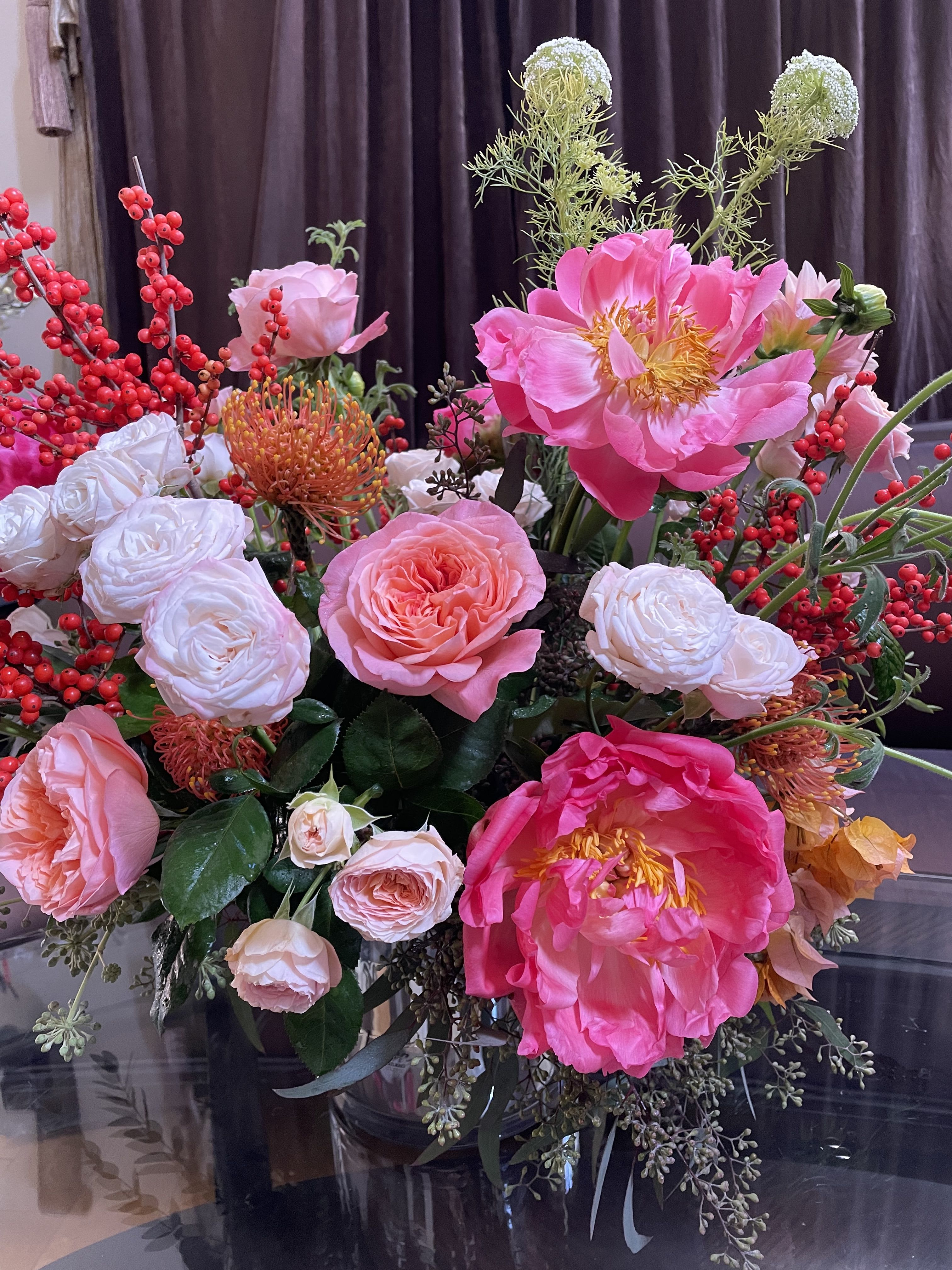 Pink and white floral arrangement with red berry branches in a glass vase