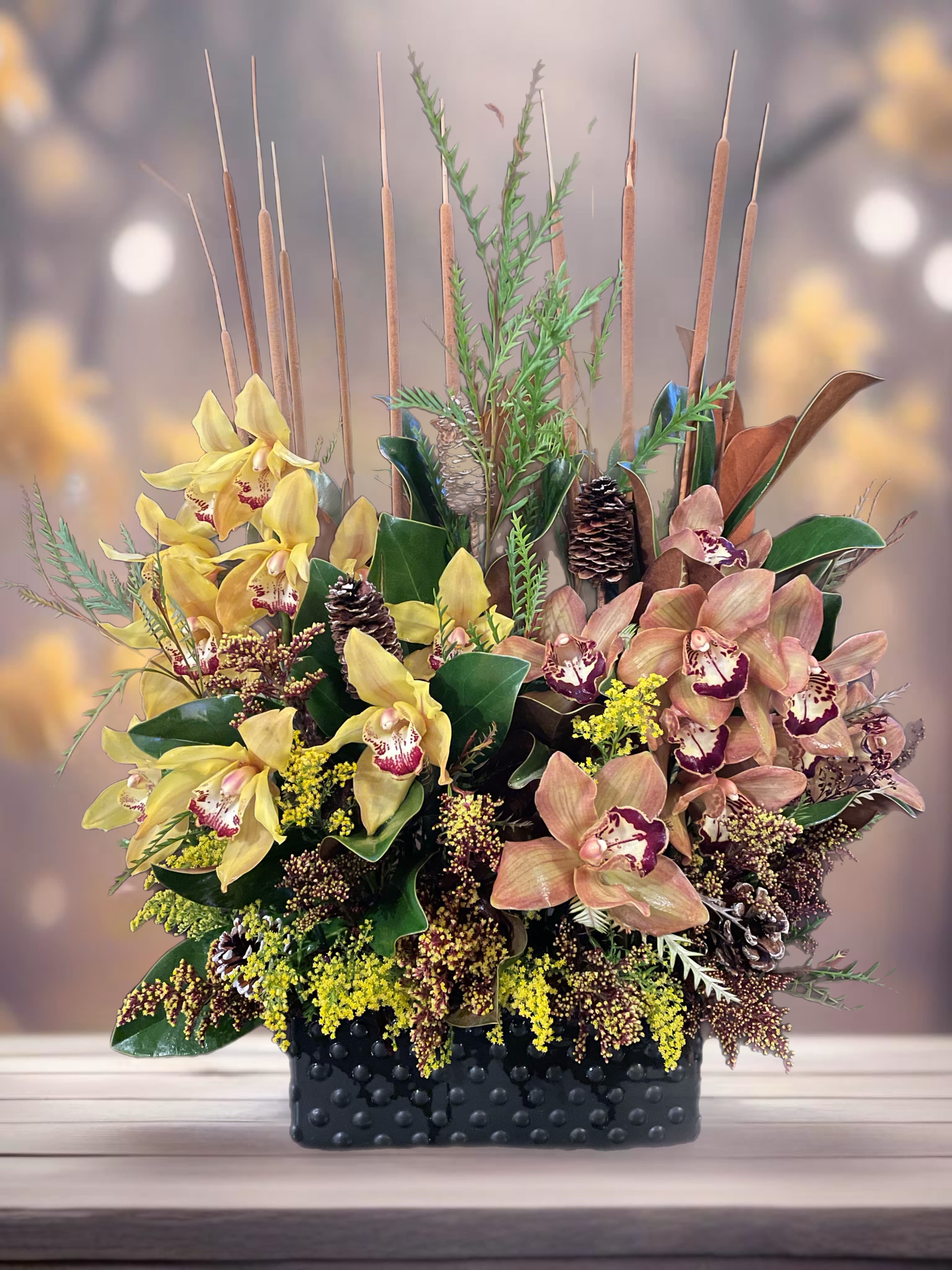 Arrangement of yellow and peach orchids in a black textured container