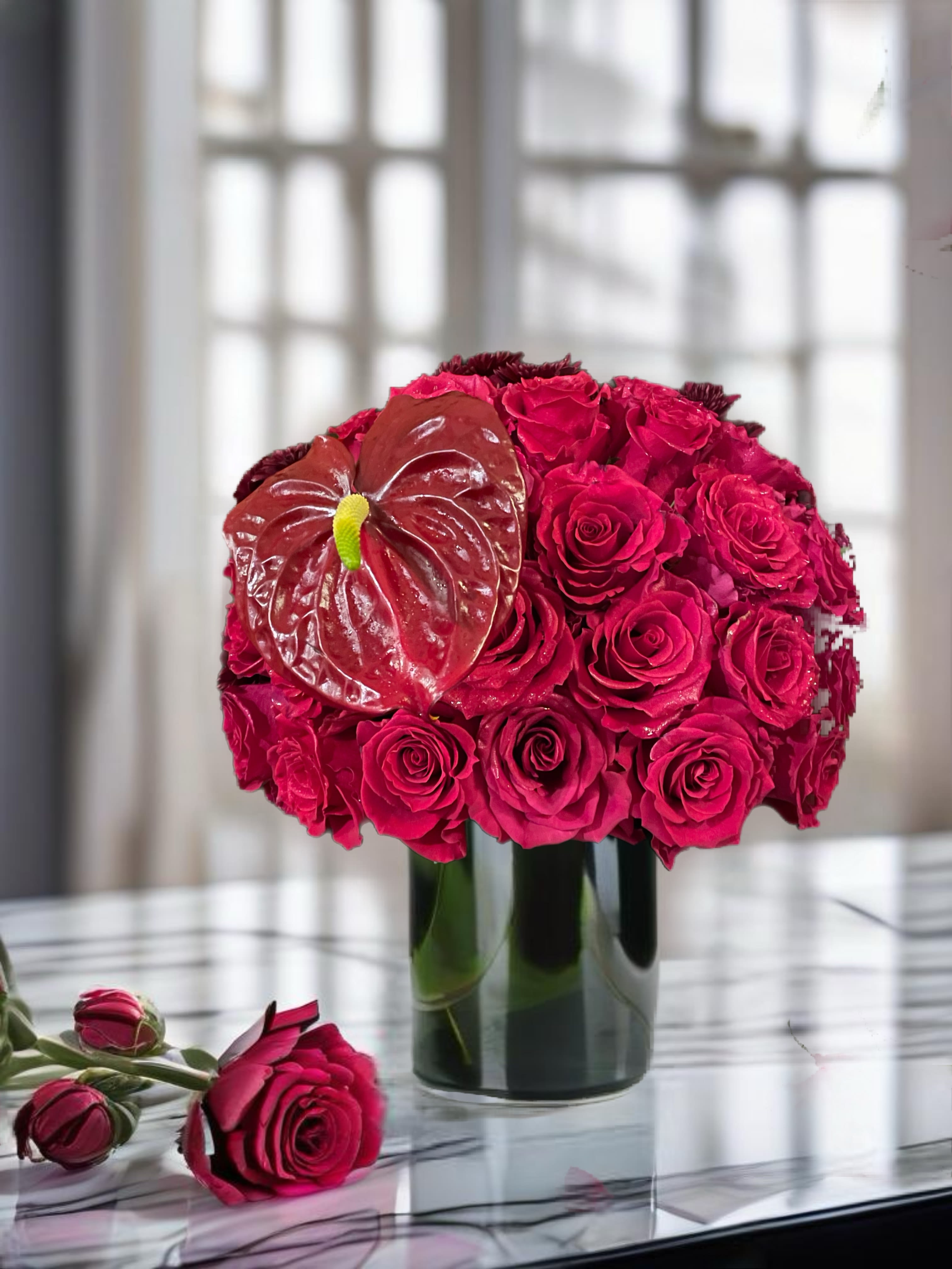 Hot pink rose arrangement in a glass vase with a red anthurium bloom