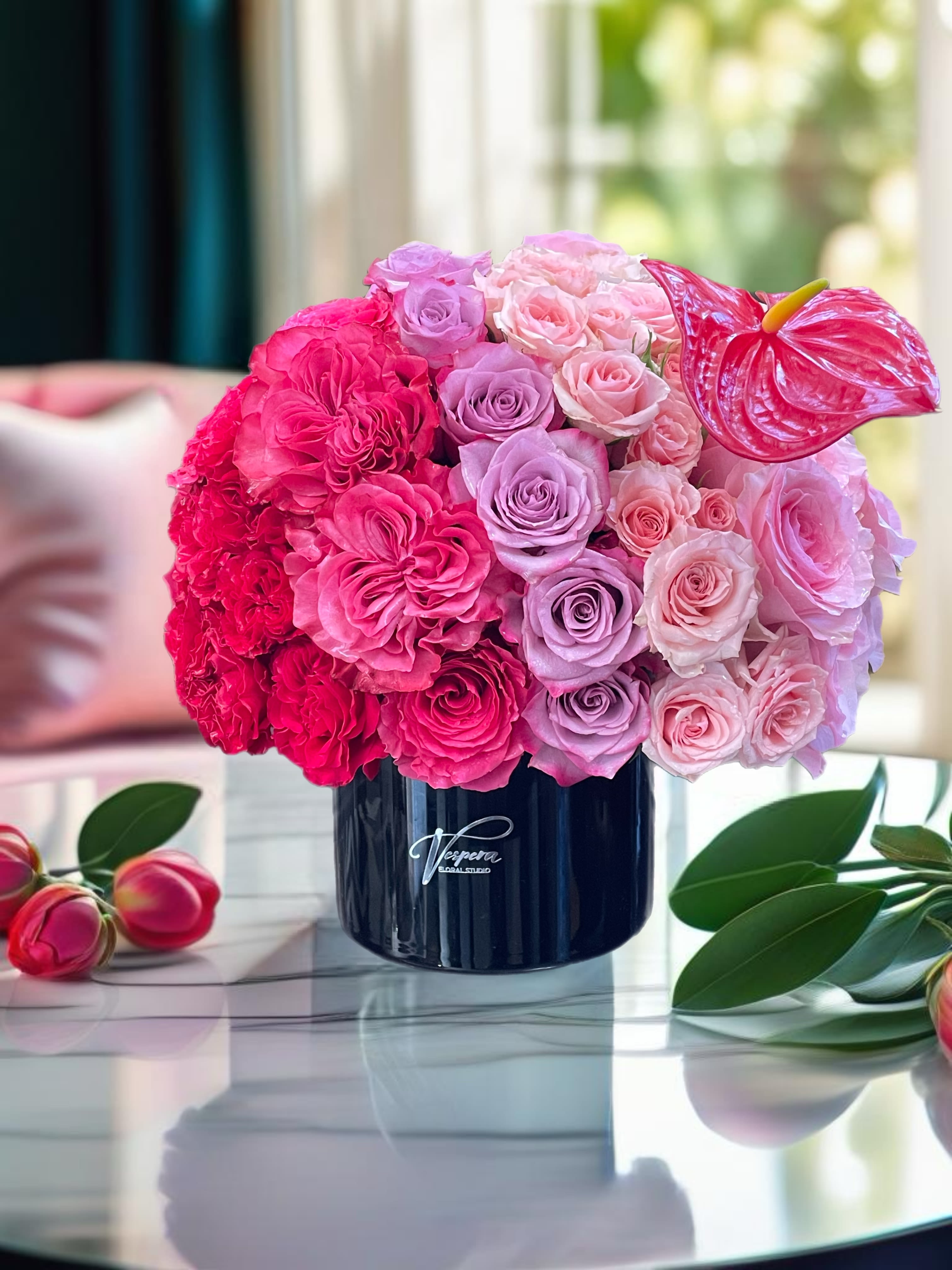 Pink and lavender rose arrangement in a dark vase with an anthurium bloom