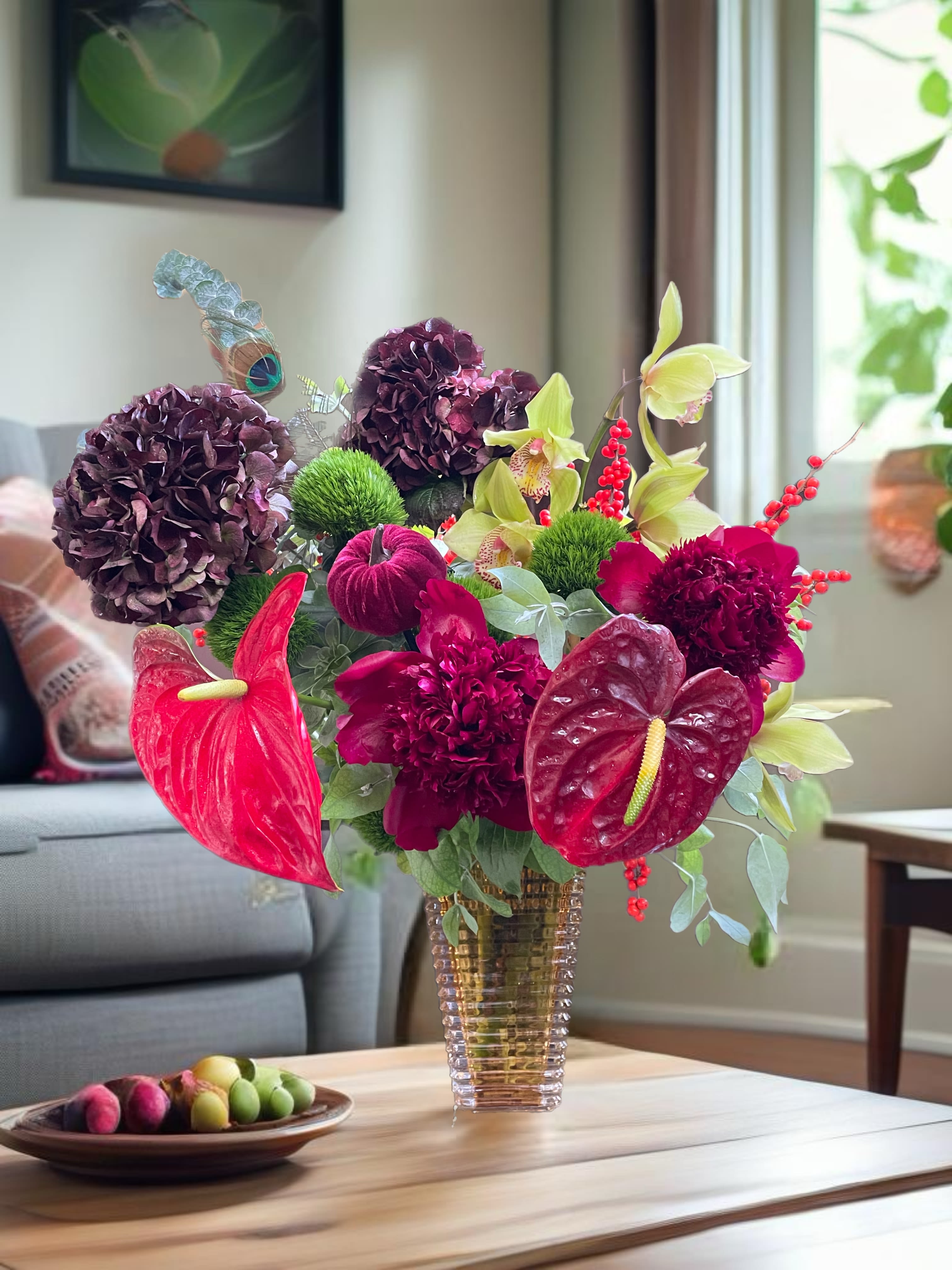 A colorful floral arrangement in a clear vase with purple blooms and red anthuriums.