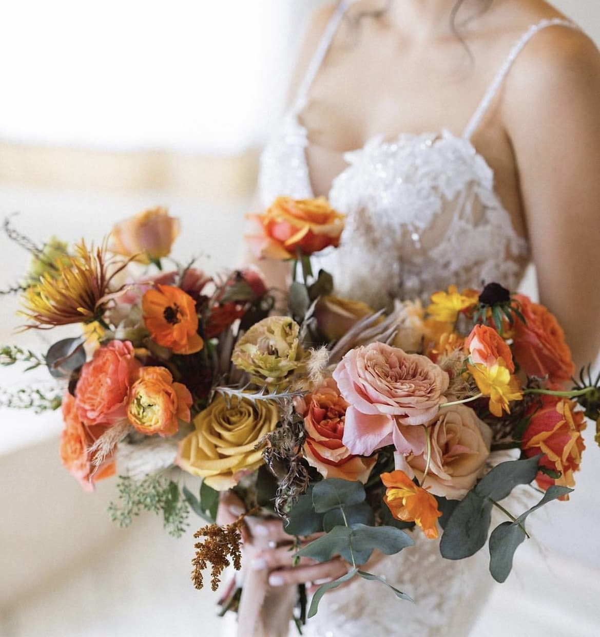 Bride holding a colorful bouquet of roses and orange blooms