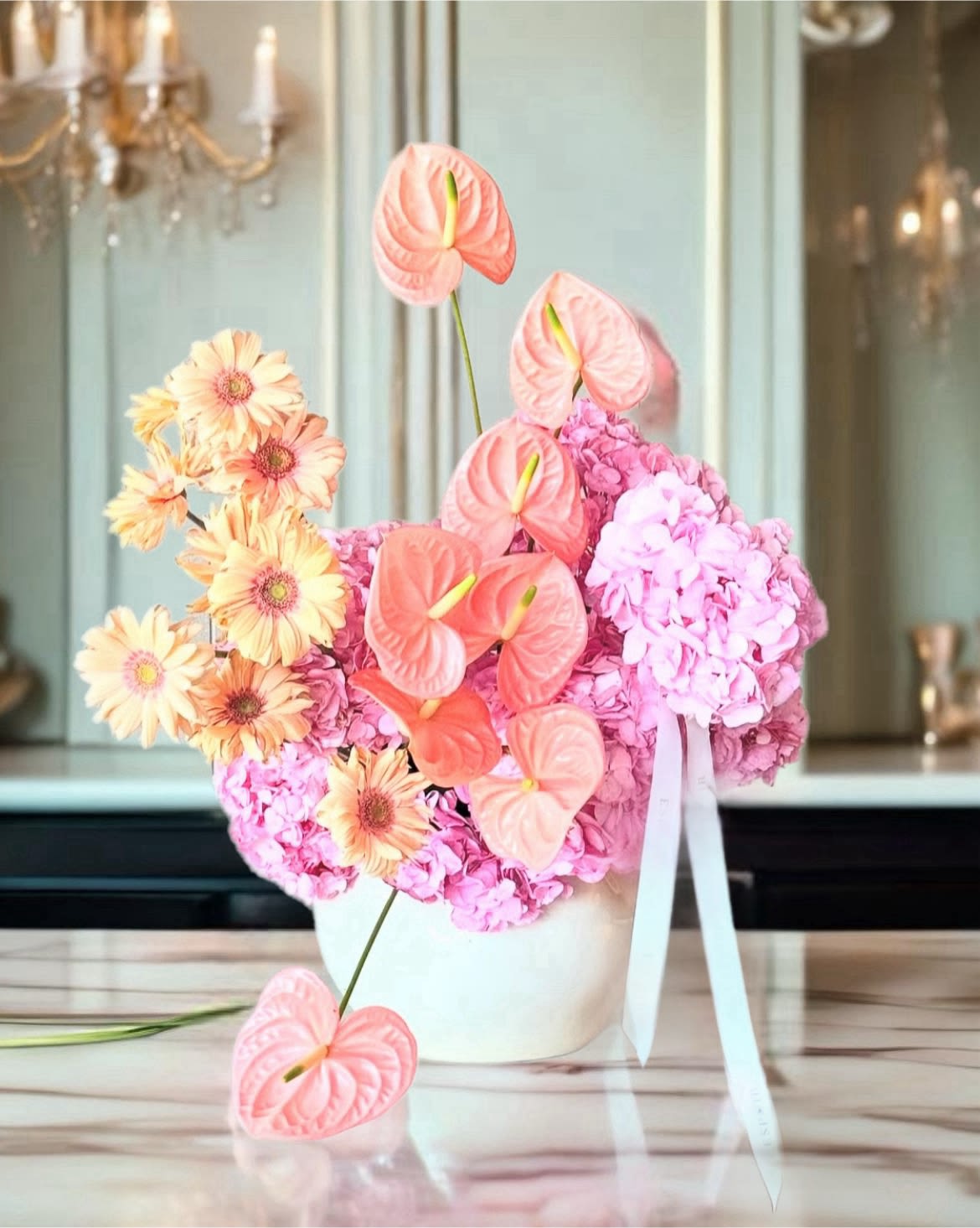 Pink and peach floral arrangement in a white vase with ribbon