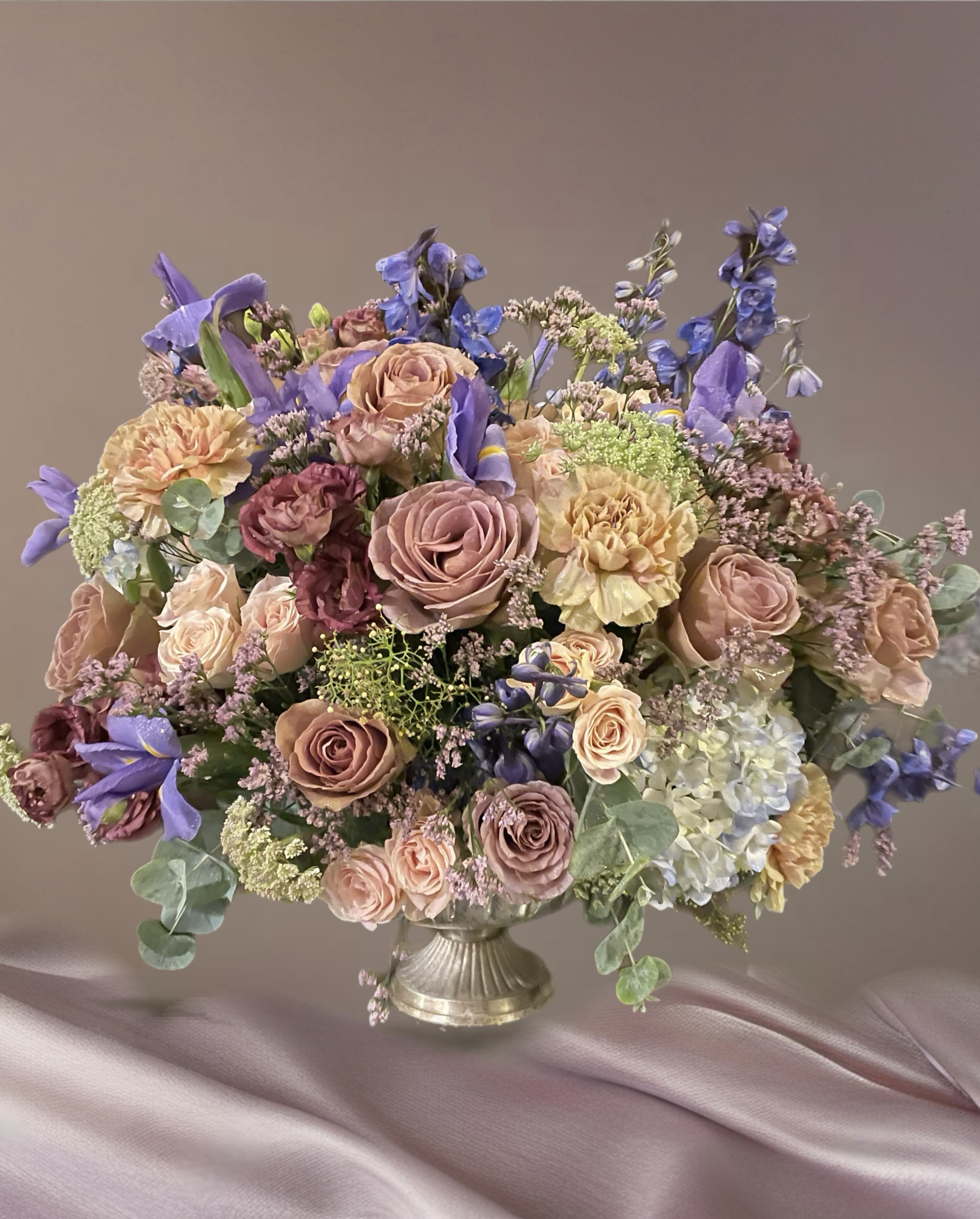 Large pastel bouquet of roses, carnations, and blue flowers in a silver vase