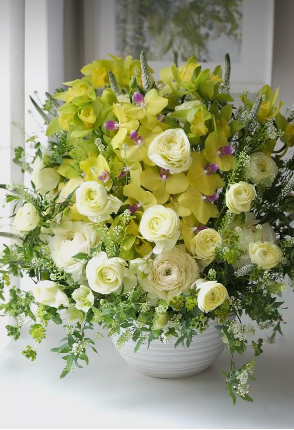 Yellow orchid and white ranunculus arrangement in a white bowl vase