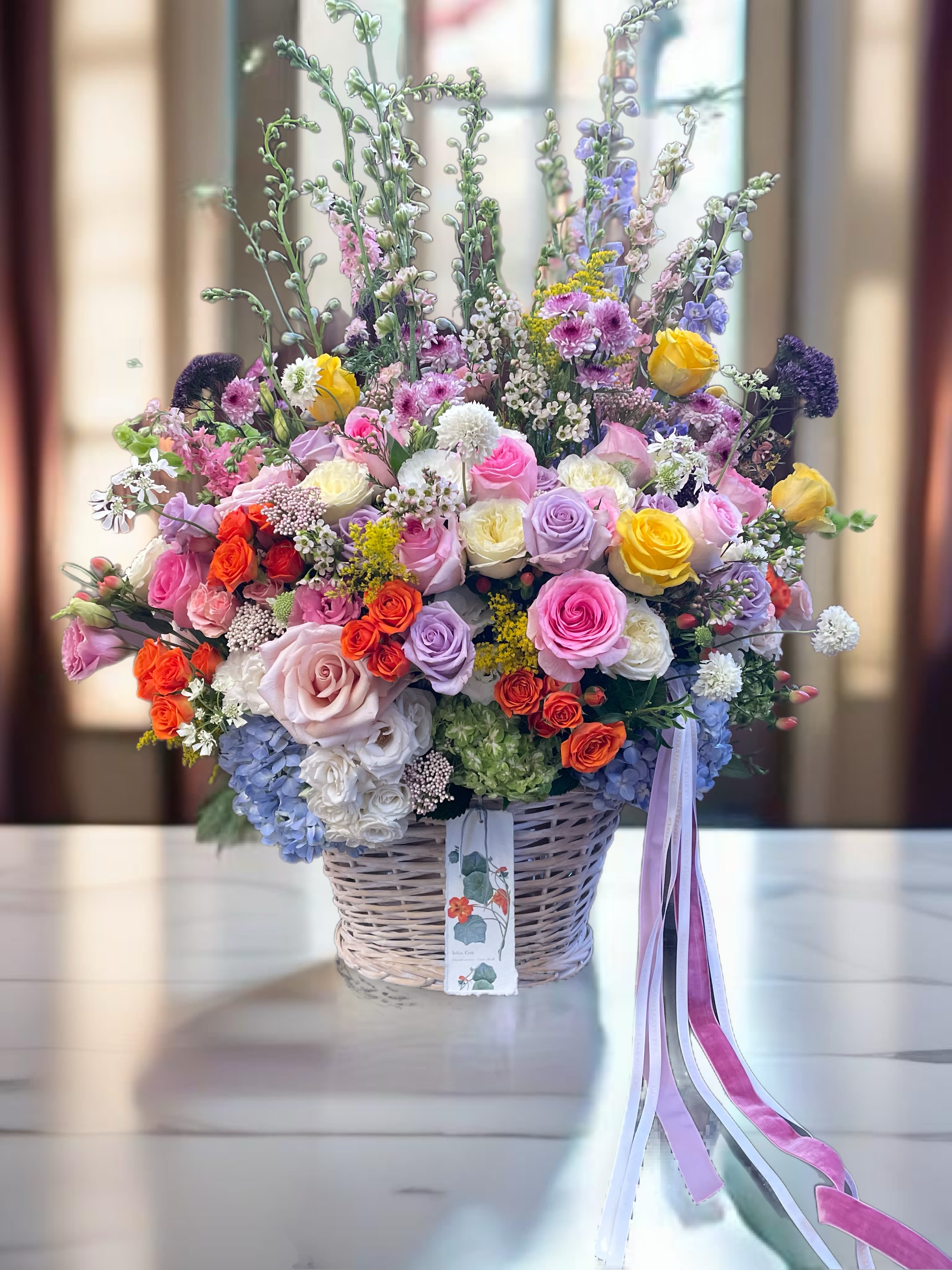 Large mixed bouquet in a wicker basket with pink, purple, yellow, and orange flowers