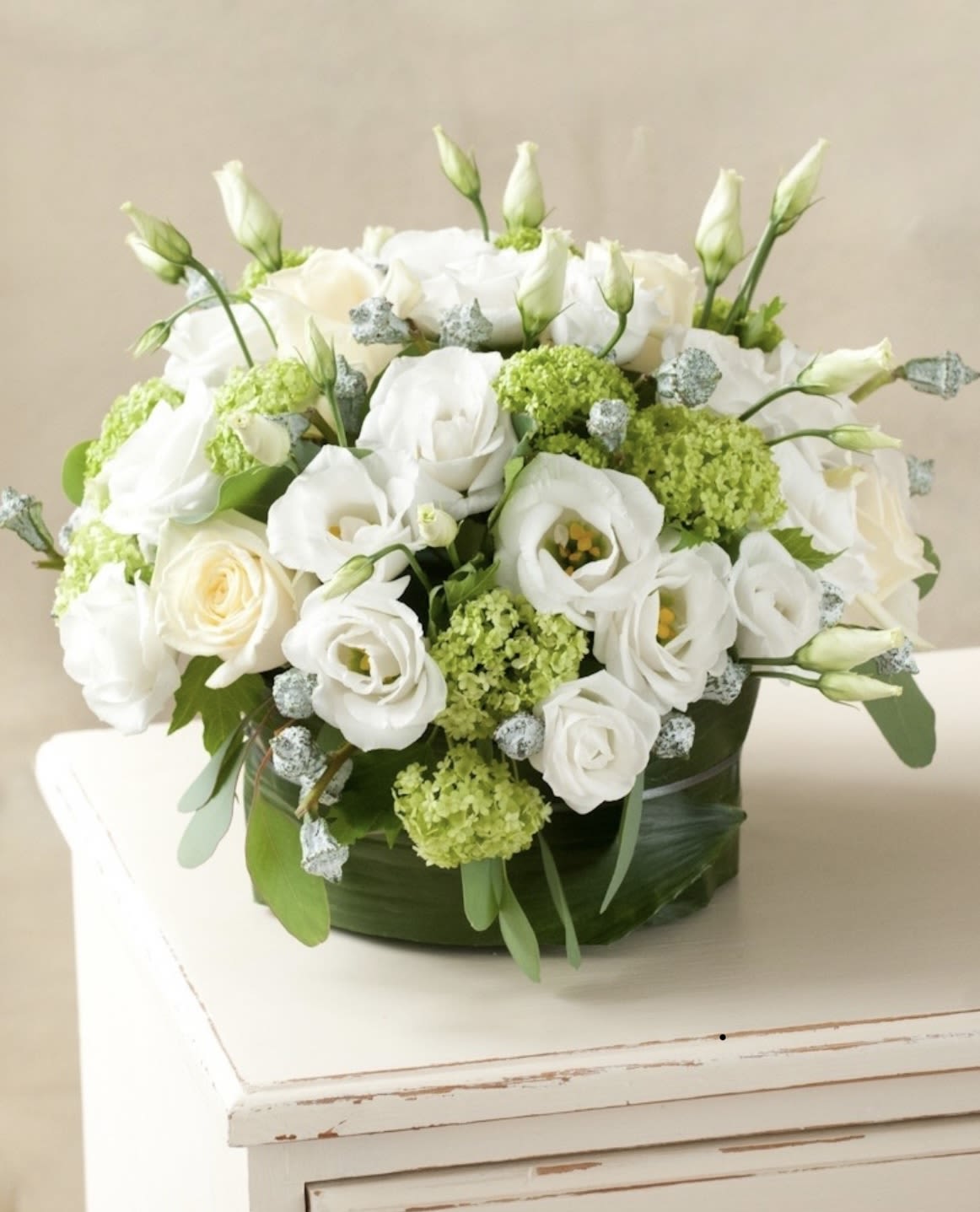 White roses and lisianthus arranged in a low round box