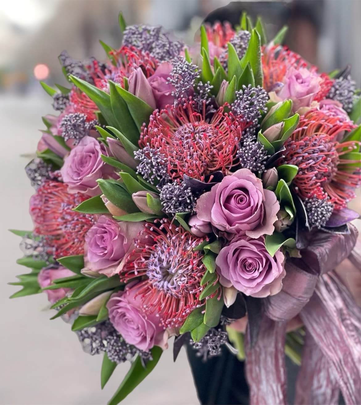Lavender roses and pink pincushion protea bouquet with green foliage