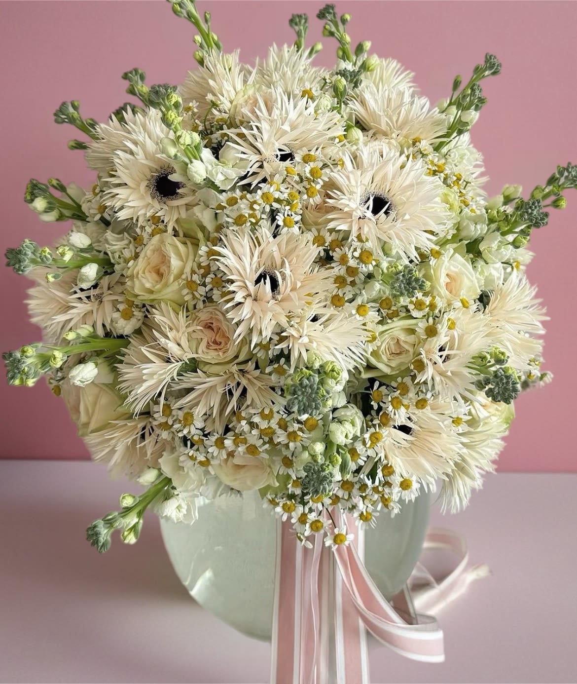 Creamy white bouquet with roses and daisy-like flowers in a pale vase