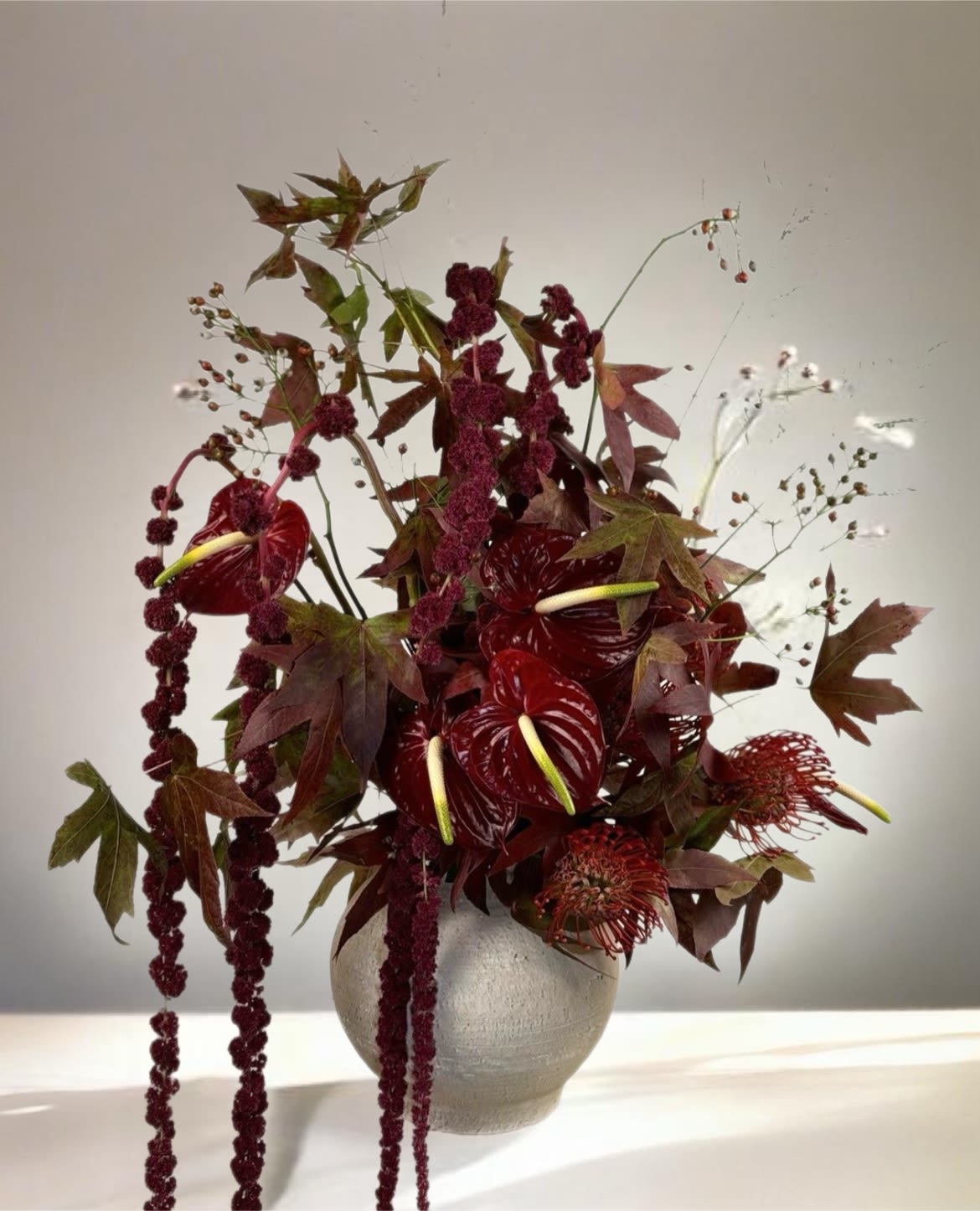 Deep red floral arrangement in a round vase with trailing burgundy blooms