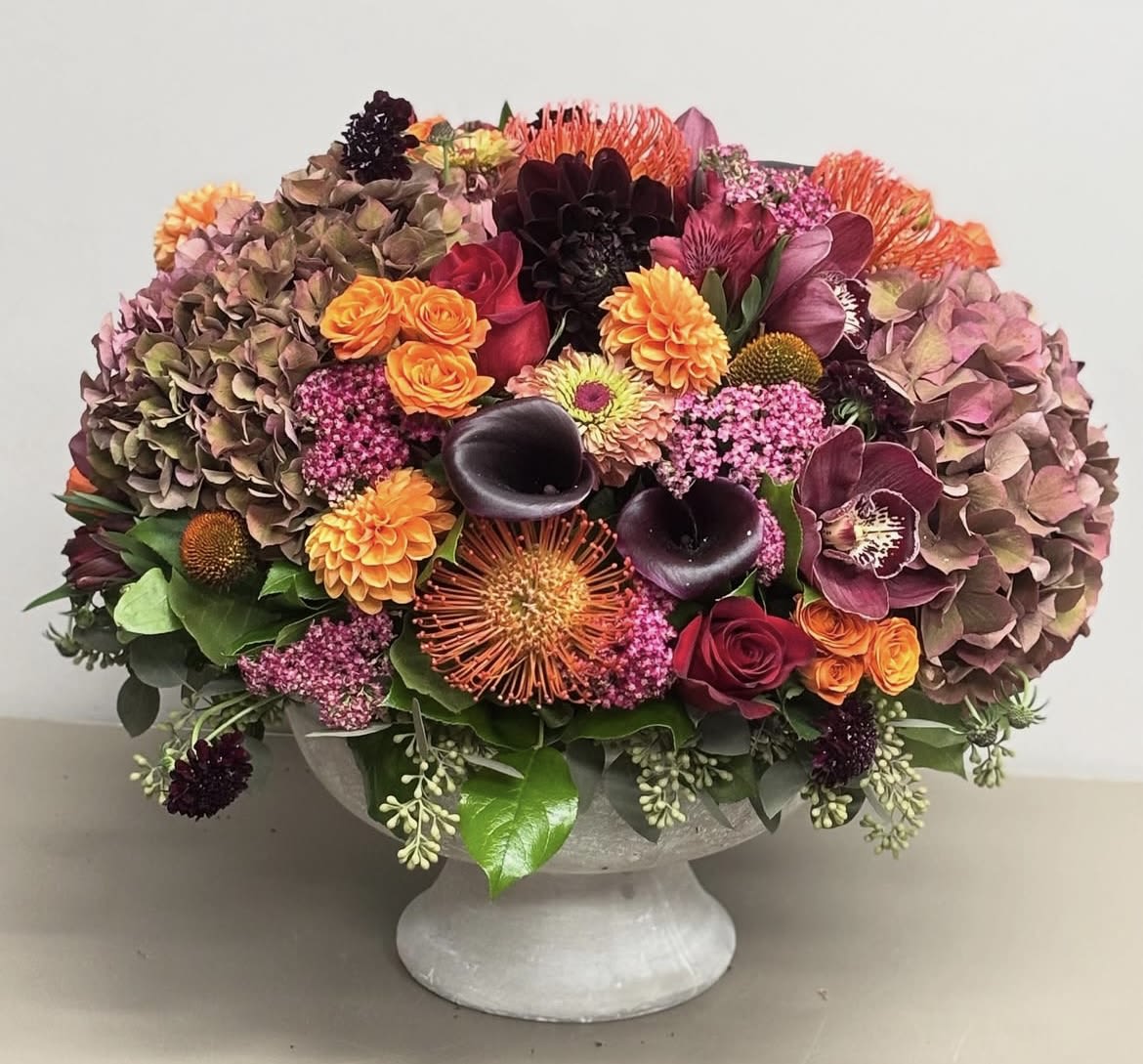 Mixed floral arrangement in a gray pedestal vase with pink, orange, and dark blooms