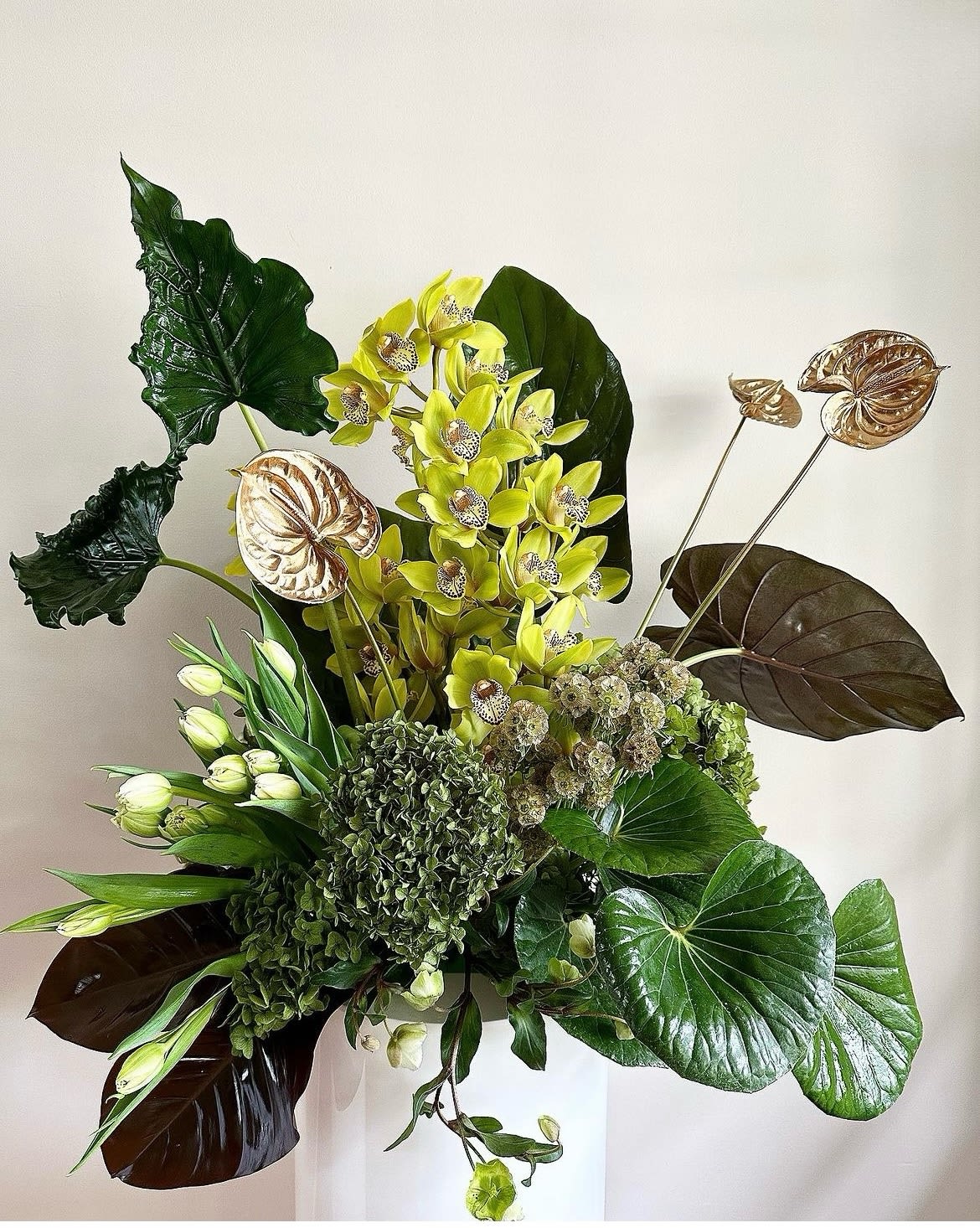 Tropical arrangement with yellow orchids and large glossy leaves in a white vase