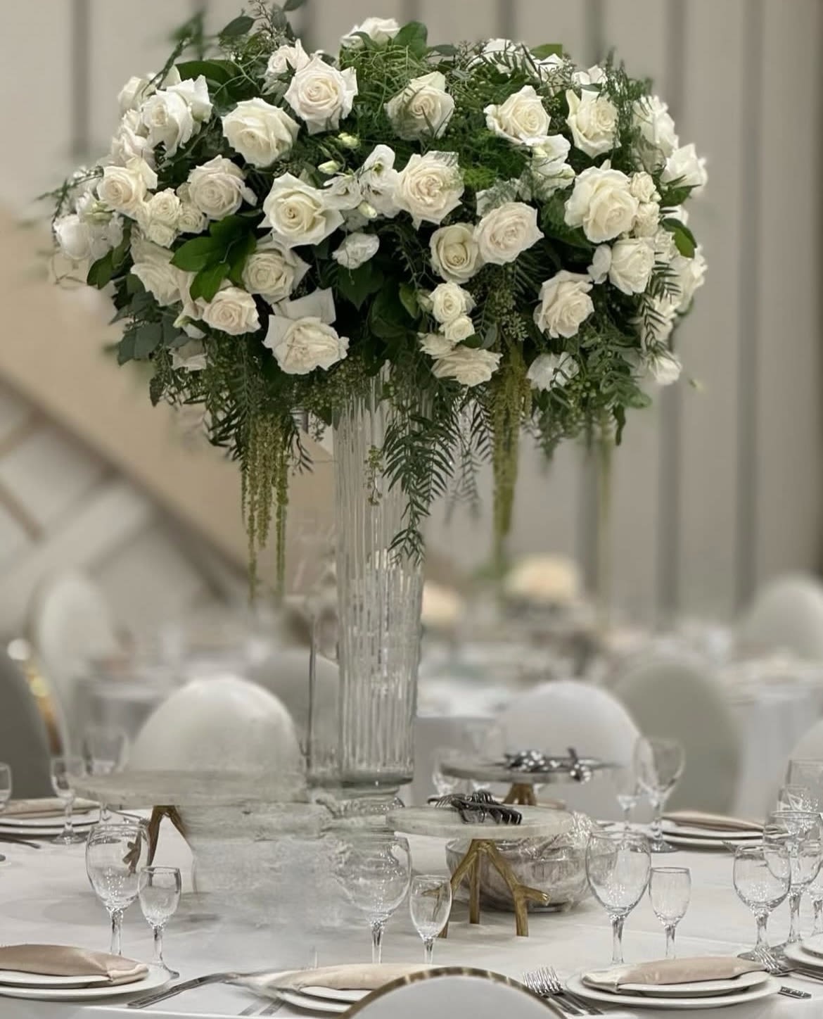 Tall white rose centerpiece in a clear glass vase on a banquet table