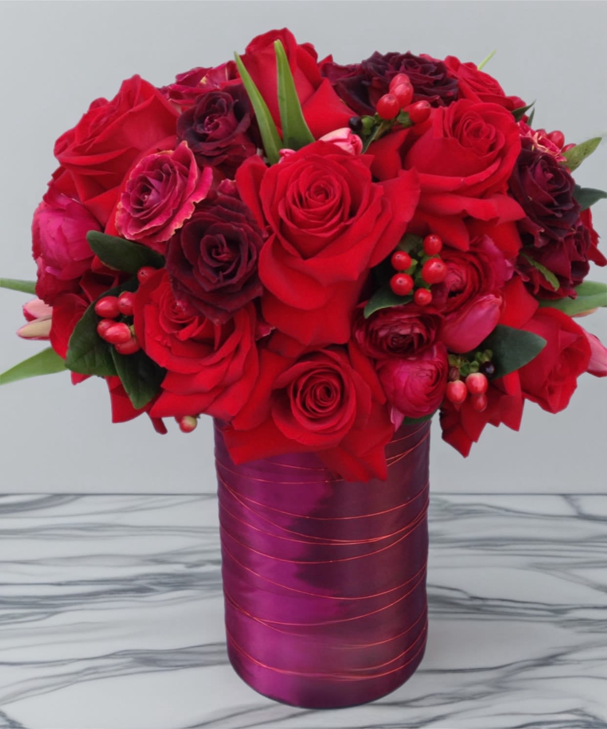 Red roses and dark burgundy blooms in a purple vase