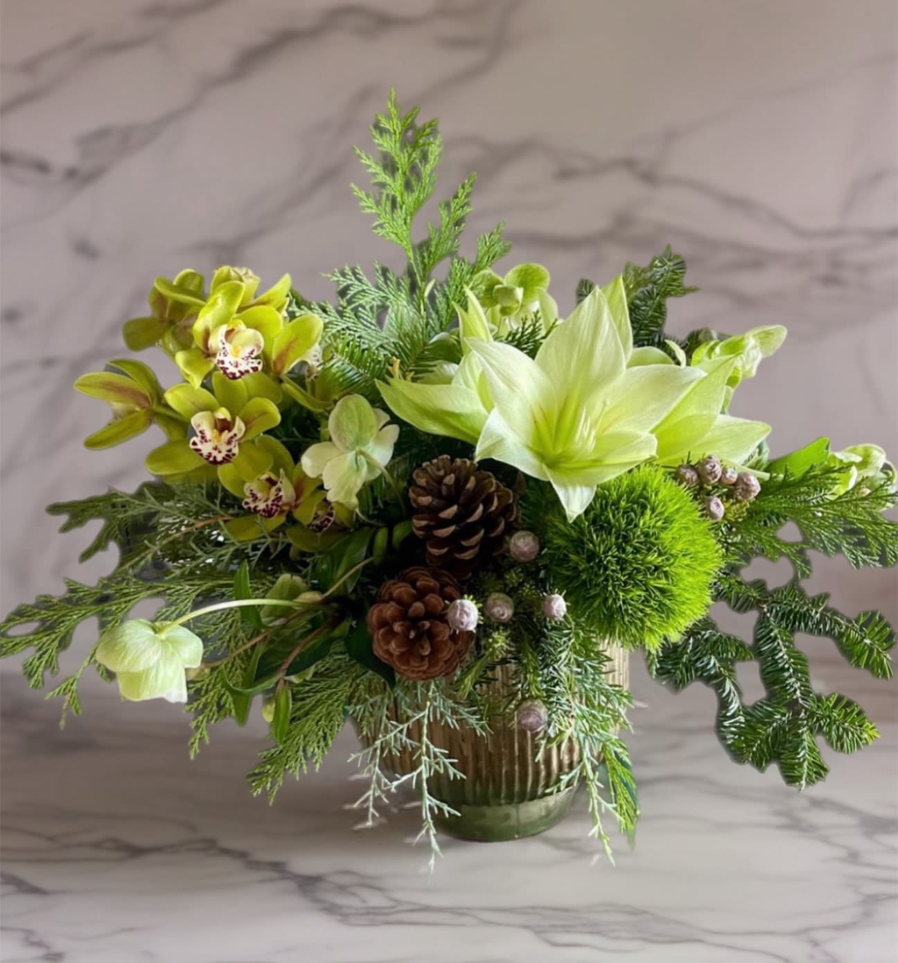 Green floral arrangement with orchids, lilies, and pinecones in a glass vase