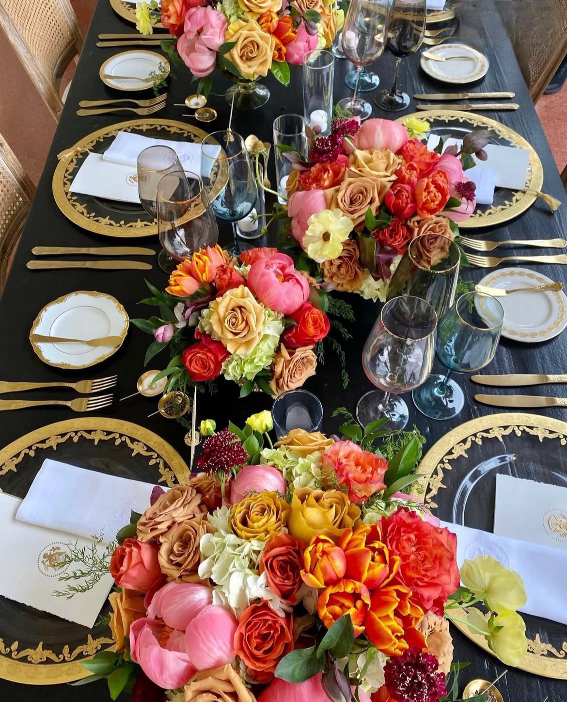 Floral centerpieces on a black-and-gold table setting with glassware and plates