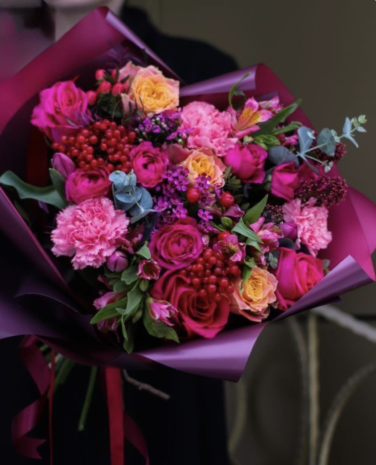 Bright bouquet of hot pink roses and carnations with yellow roses and berries wrapped in purple paper