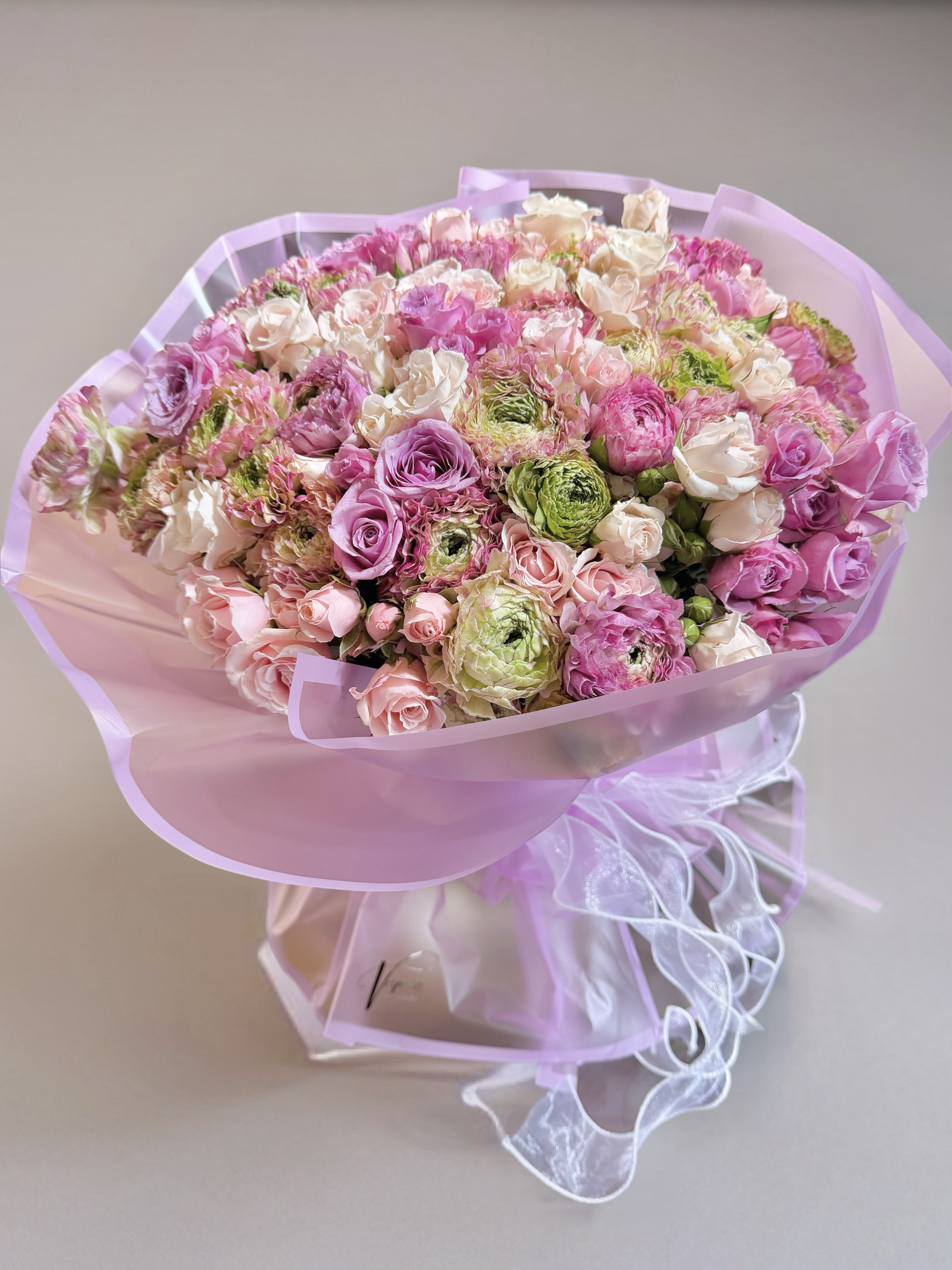 Large bouquet of pink, white, and green flowers wrapped in lavender paper