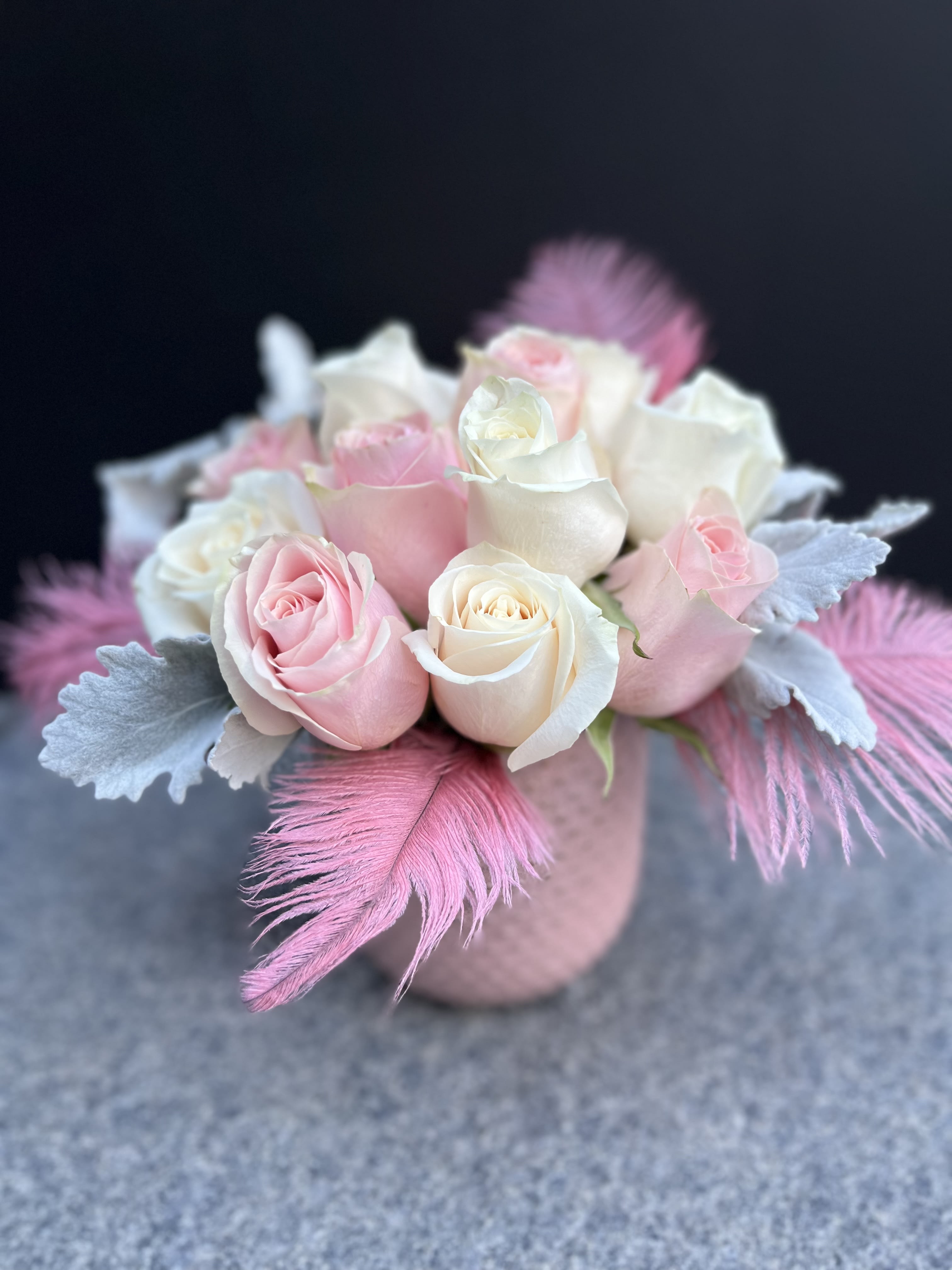 Pink and white roses arranged in a small round vase with feathers