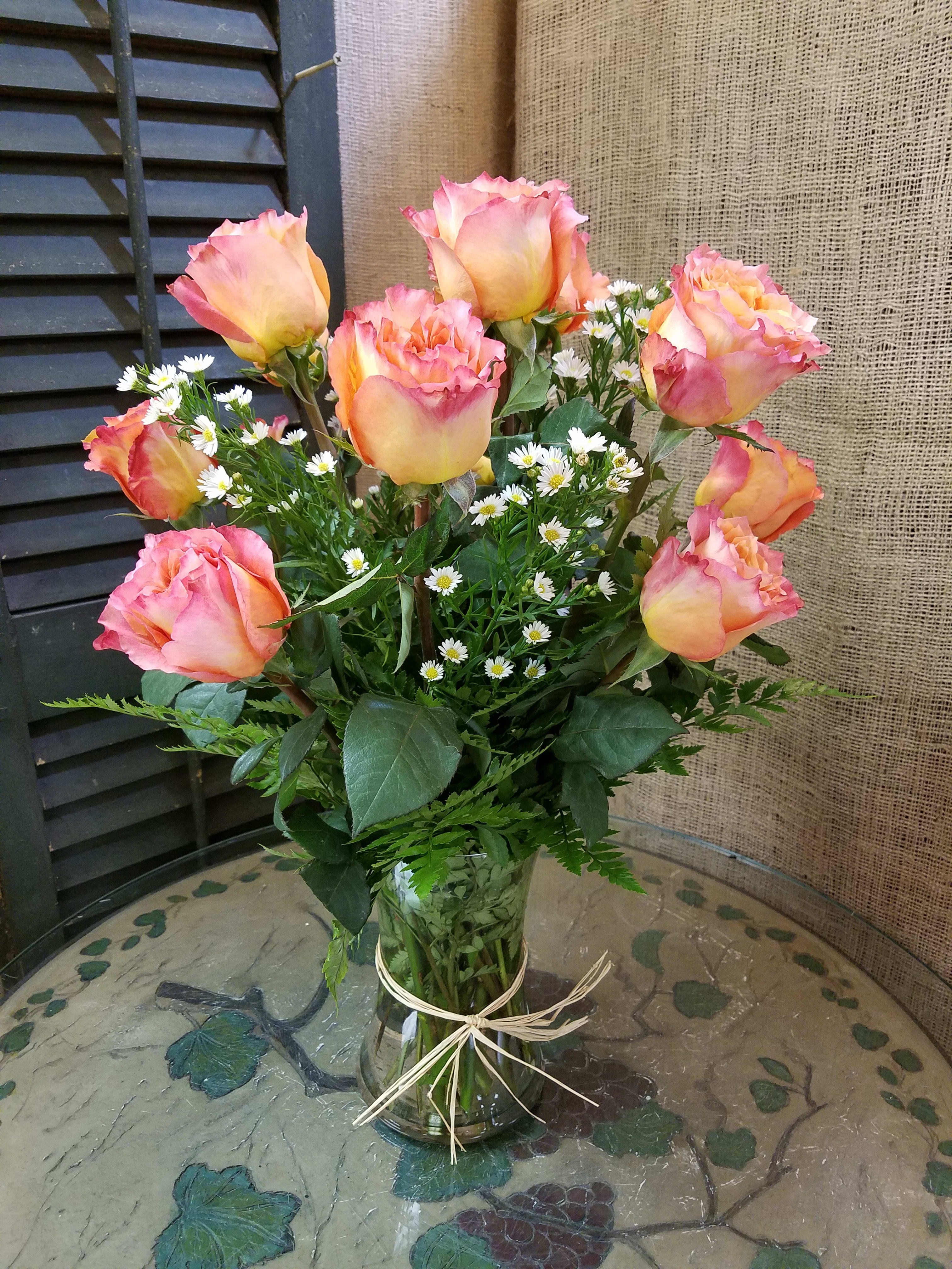 Pink and yellow roses with small white daisies in a glass vase