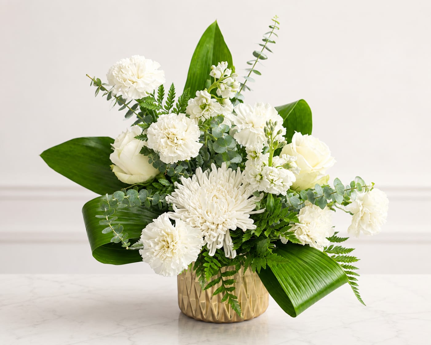 White flowers arranged in a gold vase with broad green leaves
