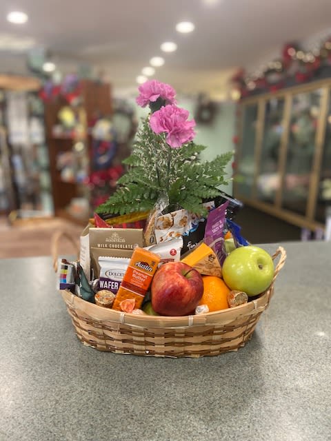 Gift basket with fruit, chocolates, and pink flowers in a wicker basket