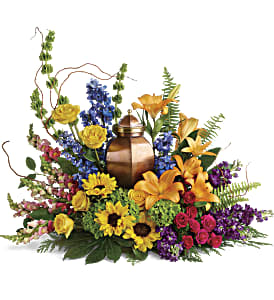 Colorful funeral urn arrangement with lilies, roses, and sunflowers