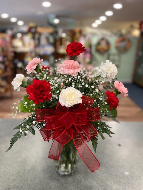 Bouquet of red, pink, and white carnations in a glass vase with a red ribbon