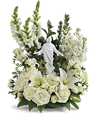 White roses and lilies arranged around a small statue in a vase