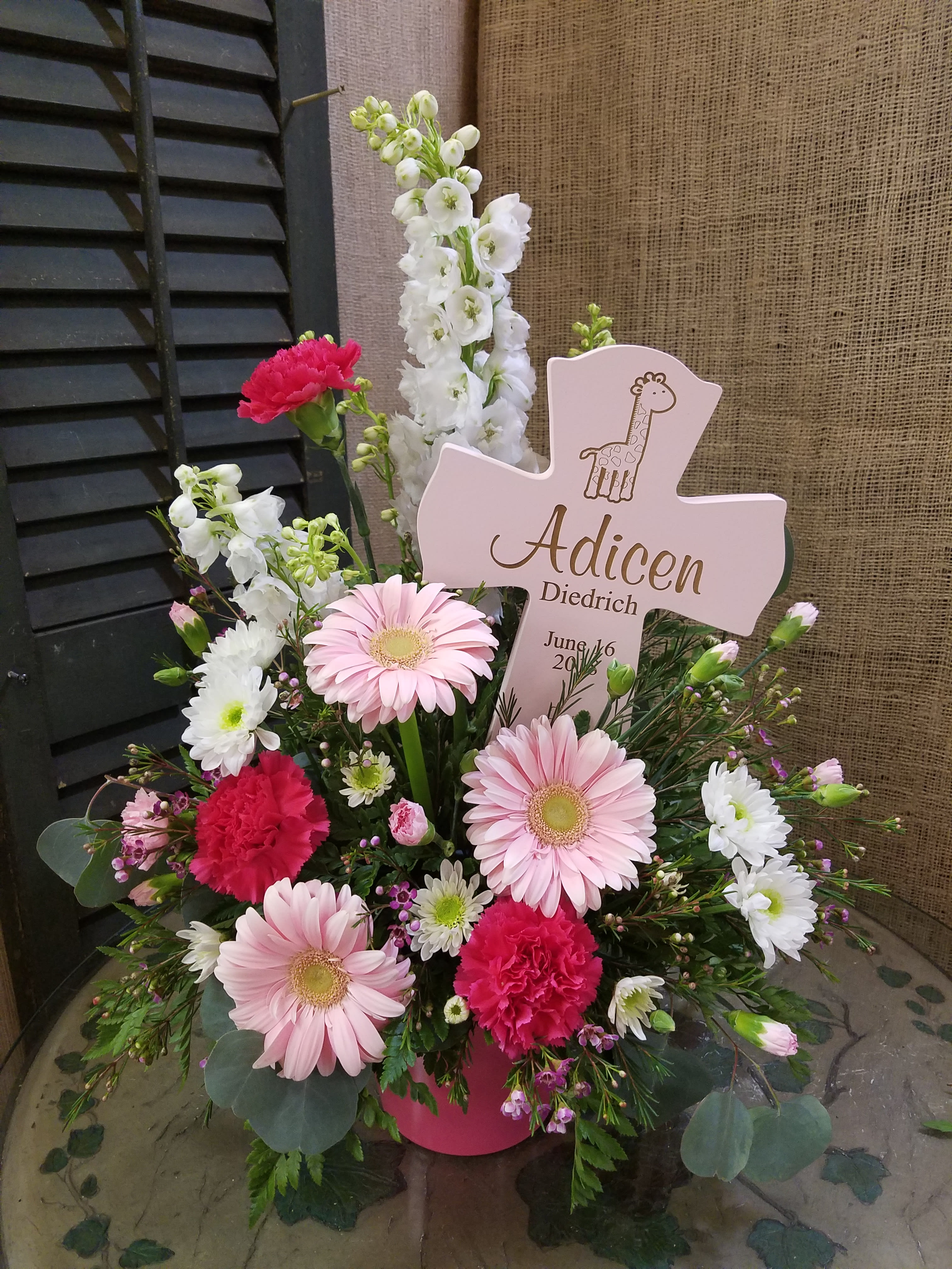 Pink and white floral arrangement with a cross-shaped sign