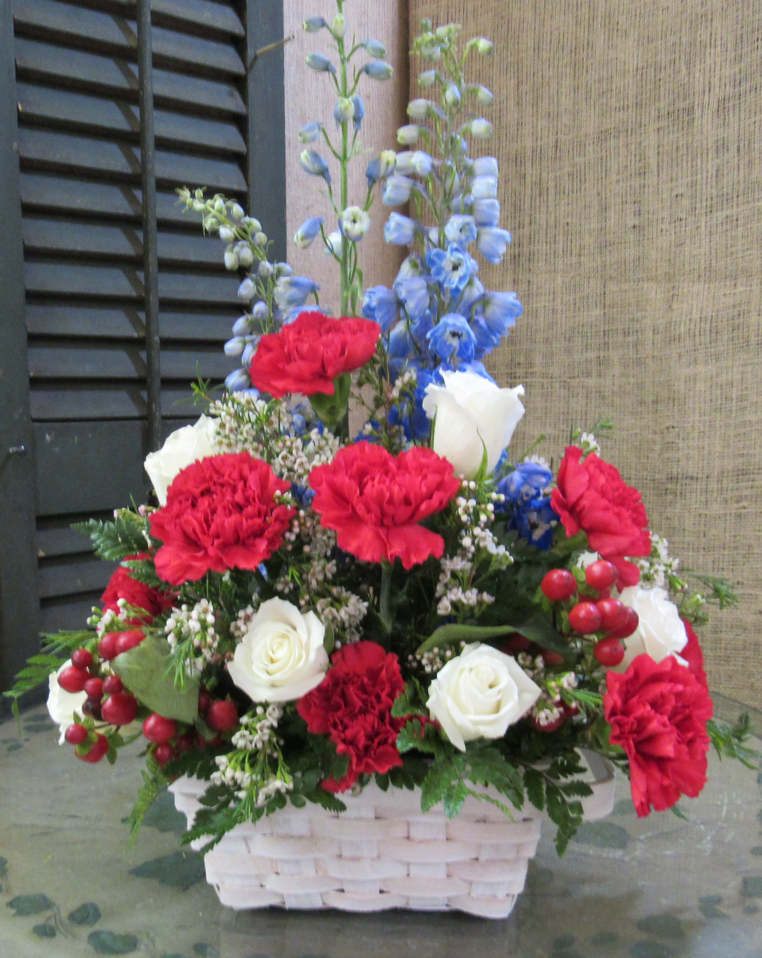 Basket arrangement of red carnations, white roses, and blue delphinium