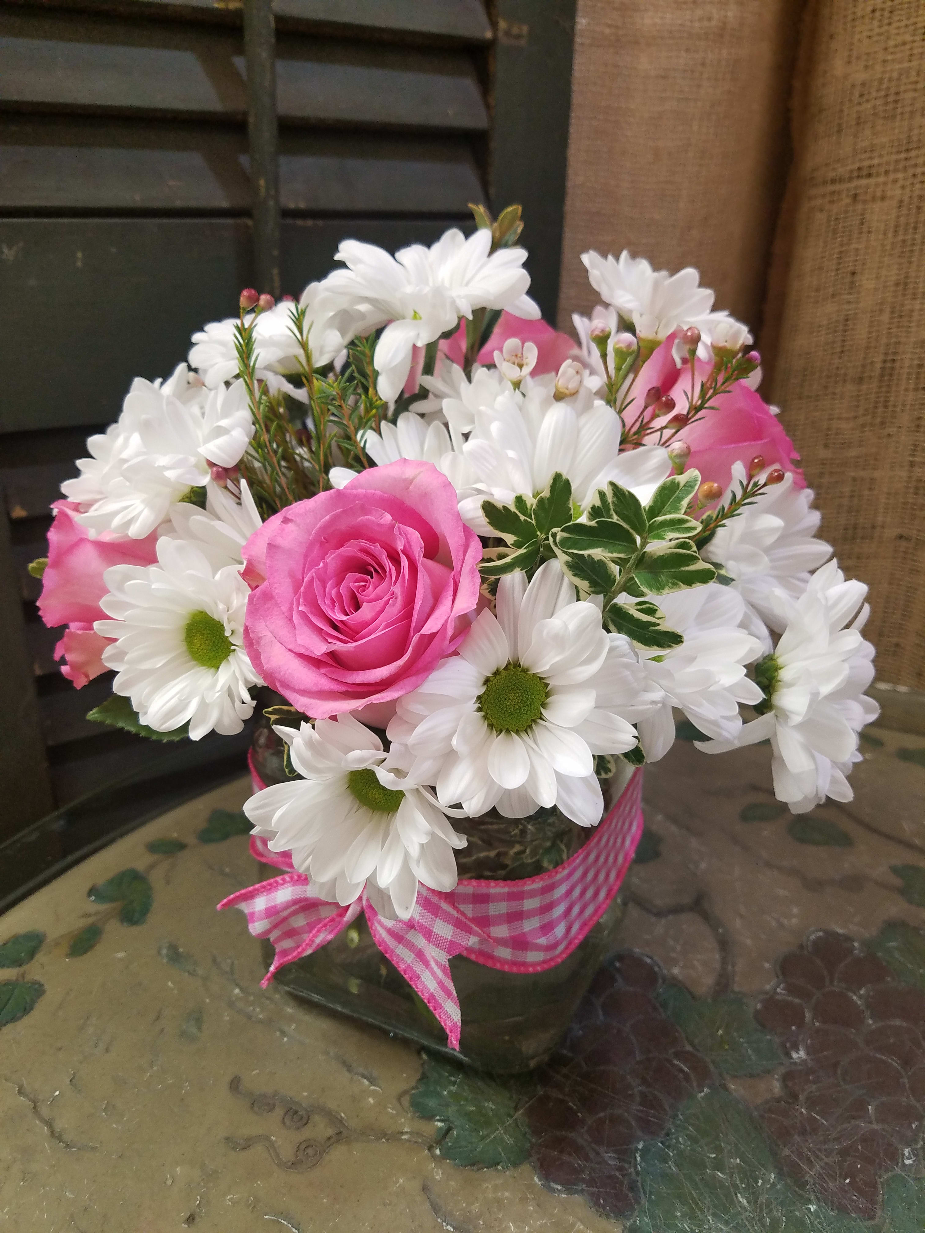 Pink roses and white daisies in a glass vase with a pink ribbon