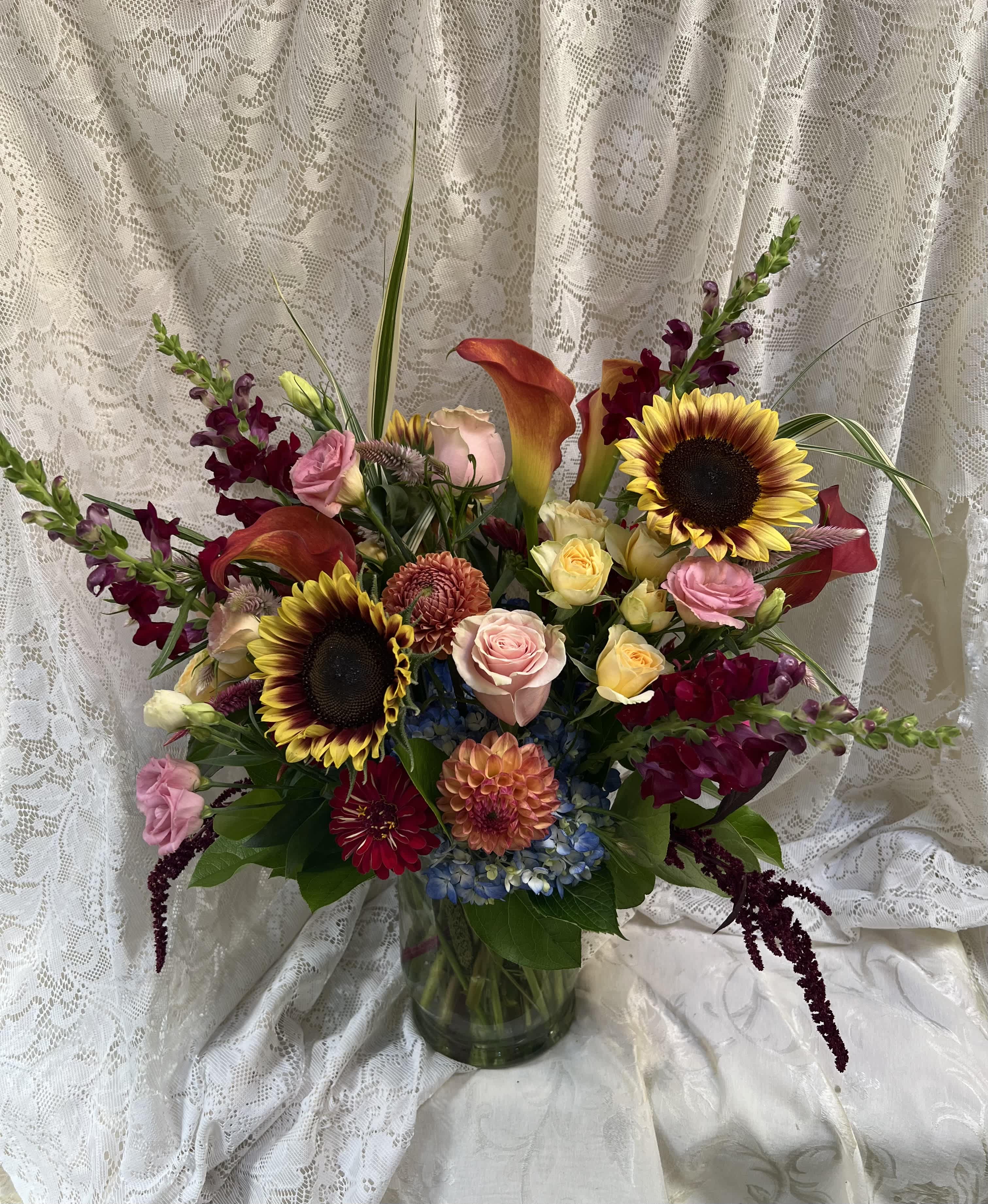 Mixed bouquet with sunflowers, roses, calla lilies, and orchids in a glass vase