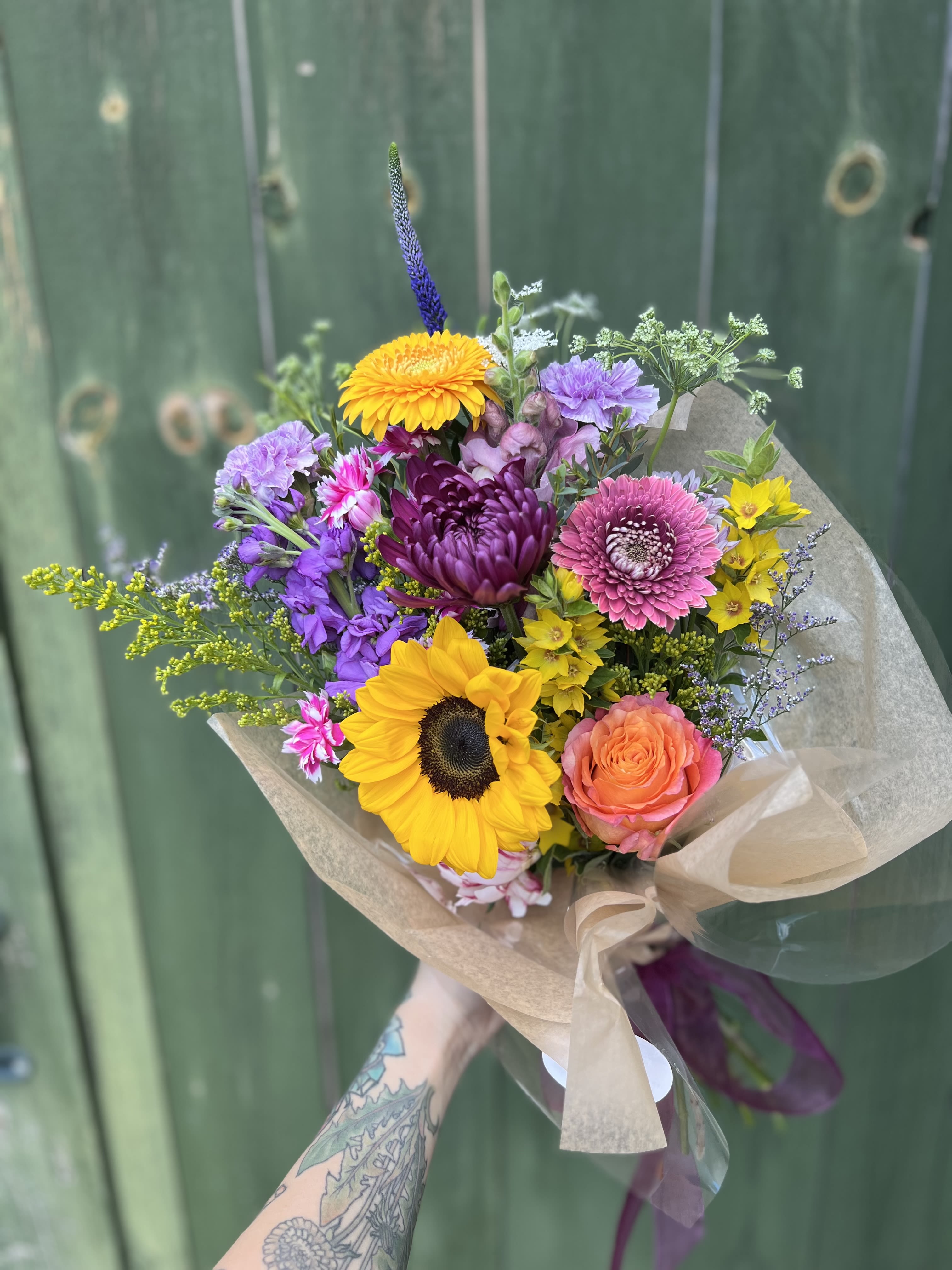 Wrapped Bouquet  - Our Wrapped Designer’s Choice Bouquet is handcrafted by our floral designers using the season’s most beautiful premium blooms. Featuring at least one rose and an artful mix of our farm fresh flowers, this bouquet embraces a wildflower-inspired style with natural movement, texture, and garden charm.  Perfect for birthdays, anniversaries, celebrations, sympathy, thank-you gifts, or simply brightening someone’s day, each bouquet is uniquely designed and wrapped with care. Finished with a beautiful ribbon bow, it arrives with a built-in water source to keep the flowers hydrated and fresh during transport, allowing for safe delivery without the need for a vase right away. 