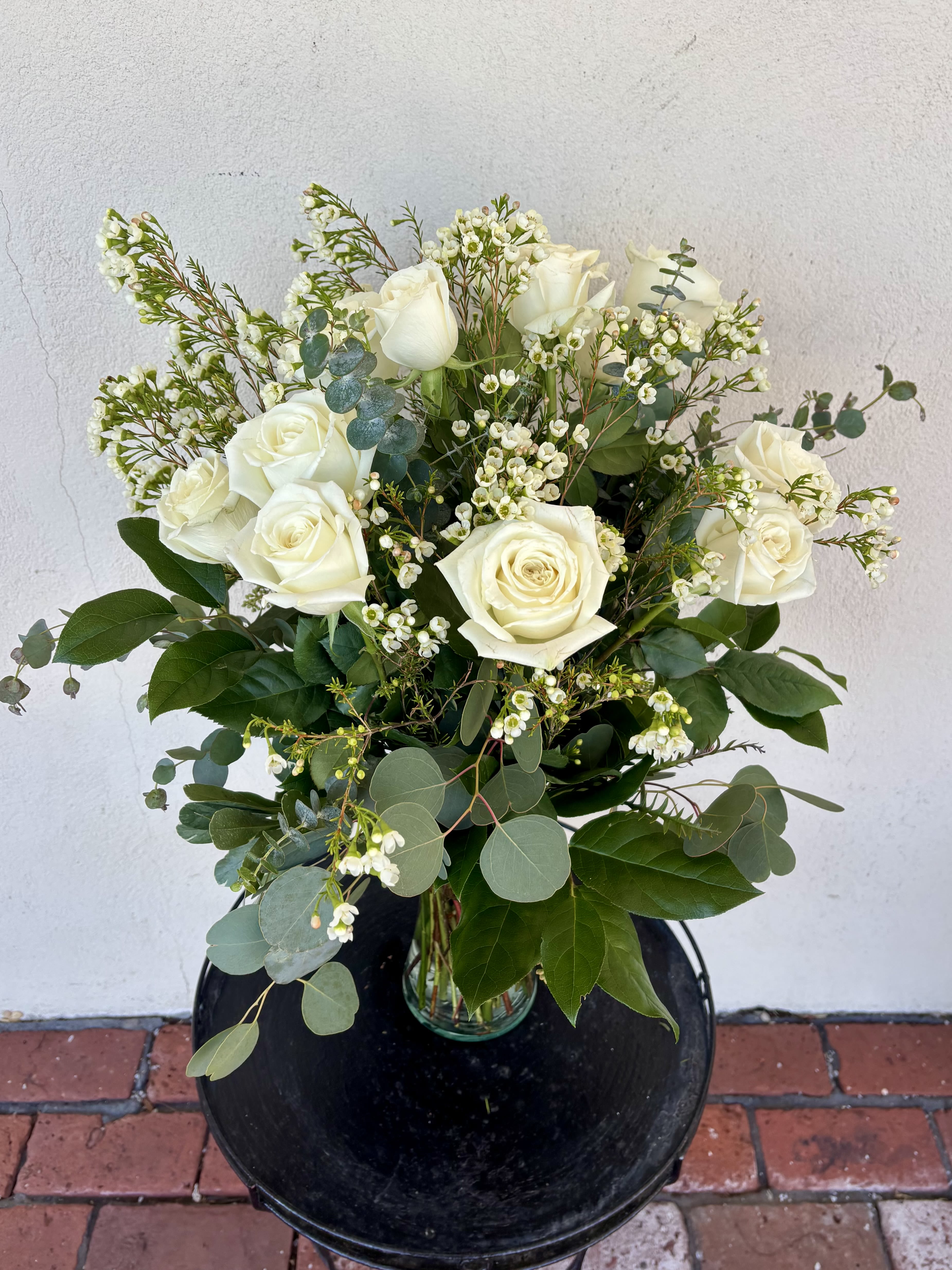 White Dozen Roses - Your choice of one dozen, one and a half, or two dozen beautiful white roses with foliage in a tall vase. Standard one dozen roses is pictured. Designer may need to make foliage substitutions based on our current inventory. Bloom Details Rose