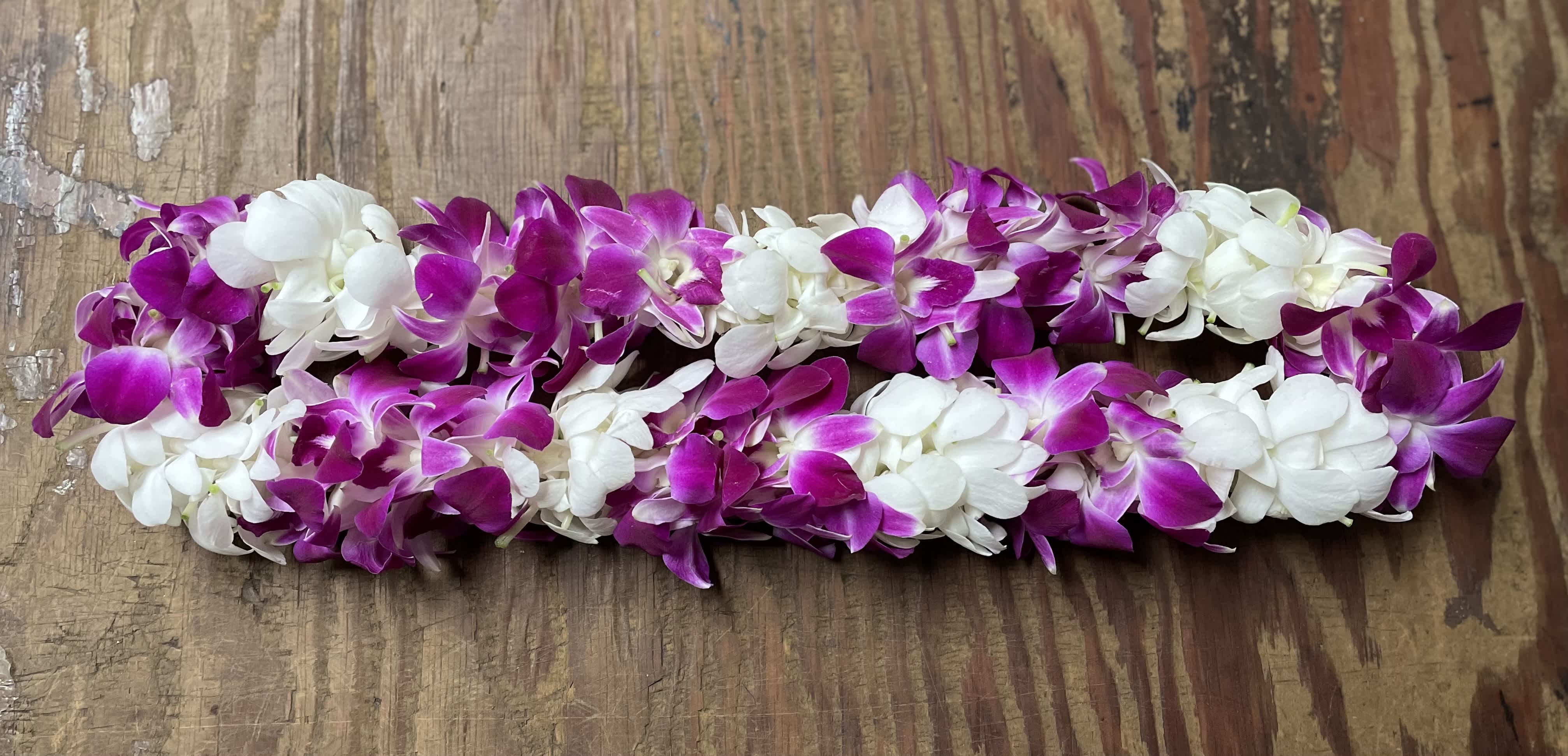 Two purple and white orchid leis on a wooden surface