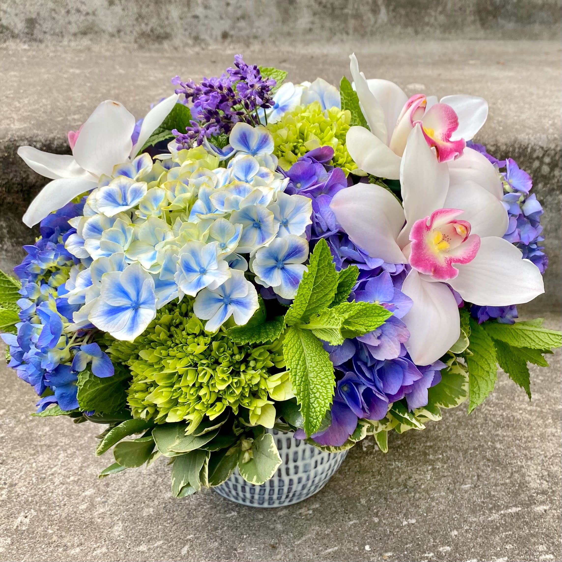 Bouquet of blue hydrangeas and white orchids in a patterned vase