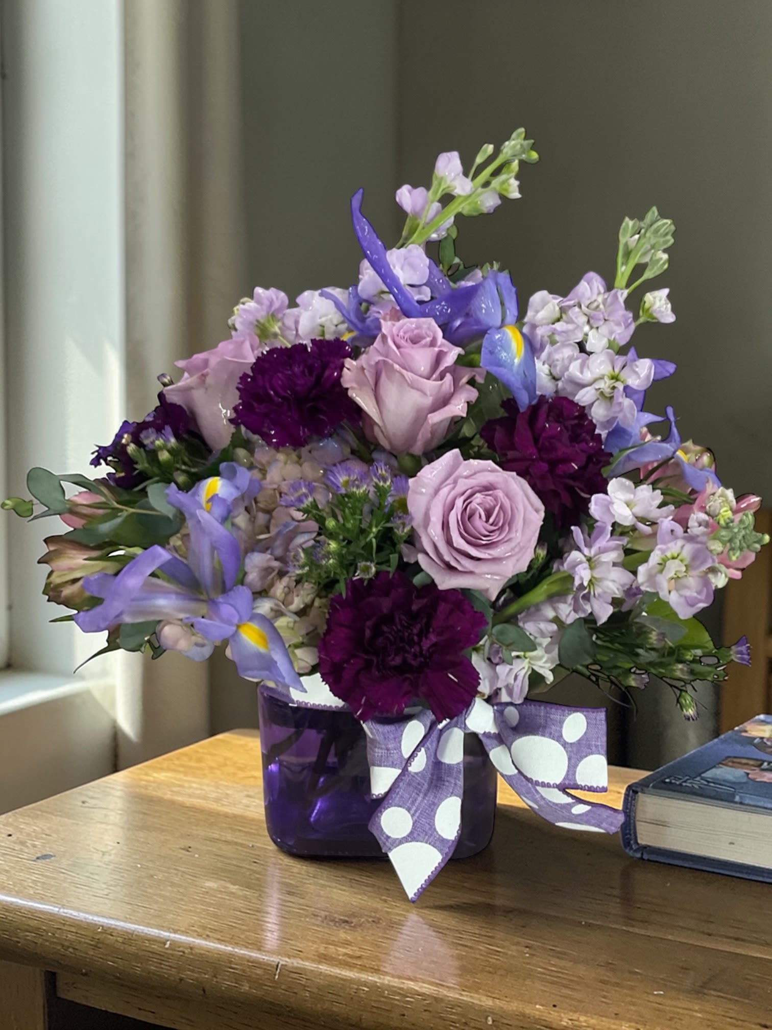 Plum Crazy - Go full-on color therapy with Plum Crazy — a lush, modern mix of lavender roses, deep plum carnations, fragrant stock, and striking blue iris gathered in a rich purple glass vase. Soft pastels meet bold jewel tones in a design that feels playful, elegant, and just the right amount of dramatic.  This is the kind of arrangement that doesn’t sit quietly in a room — it changes it. Whether it’s a birthday surprise, an anniversary, a thank-you, or just because someone needs a lift, Plum Crazy delivers color, energy, and a little bit of wow the second it arrives.  Designed in-house with a balanced mix of texture, movement, and layered color, this piece leans into that effortless, natural look while still feeling polished and intentional.  Flowers may vary slightly based on availability, but the signature plum, lavender, and purple palette will always remain true to the overall style.  Available for local flower delivery through Aspen Tower Florist, serving Greensburg and Shelbyville along with Rushville, Batesville, Westport, Oldenburg, St. Paul, Waldron, and Milroy surrounding areas. 