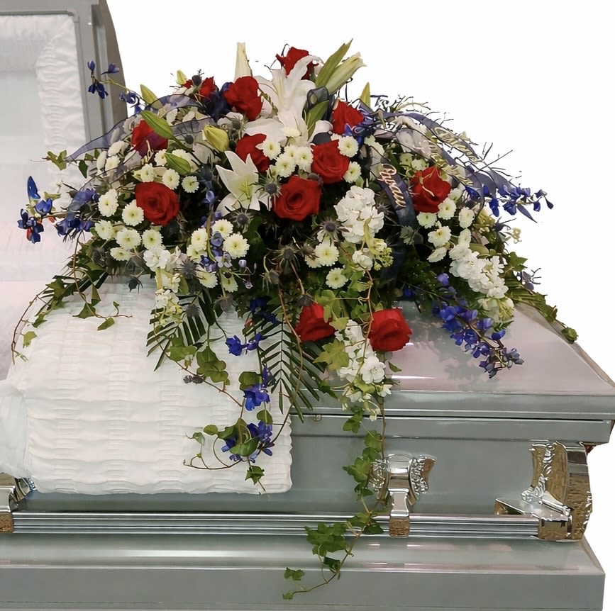Freedom’s Tribute Casket Spray - Bold, patriotic, and deeply meaningful, Freedom’s Tribute is a red, white, and blue casket spray created to honor a life of service, sacrifice, and devotion. Rich red roses, elegant white lilies, brilliant blue delphinium, and complementary blooms are arranged with flowing greenery to create a tribute that is both powerful and dignified.  Designed to rest gracefully across the casket, this piece combines strong patriotic colors with natural movement and texture, reflecting honor, courage, loyalty, and love of country. It is an especially meaningful choice for veterans, active-duty military personnel, first responders, and those whose lives were defined by service to others.  This design was originally created exclusively for a family served through Todd Funeral Centre &amp; Crematory, 1600 S State Road 3, Rushville, IN 46173. Families may learn more about Todd Funeral Centre &amp; Crematory at www.toddfuneralcentre.com.  Customers can view additional examples of our custom casket sprays in the Casket Spray section of our website, including real photographs and videos of funeral tributes created by Aspen Tower Florist.  Thoughtfully designed and professionally arranged, Freedom’s Tribute serves as a lasting expression of gratitude, respect, and remembrance—a powerful farewell for a life lived with purpose, dedication, and honor.