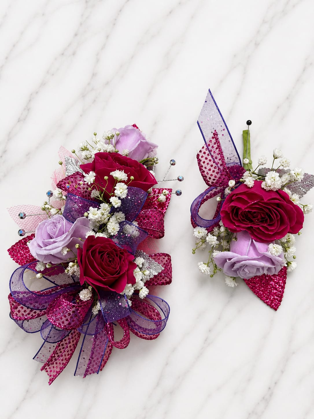Magenta Magic Formal Set - MAGNETIC BOUTONNIERE WARNING: CONTAINS STRONG MAGNETS. DO NOT USE IF YOU HAVE A PACEMAKER, DEFIBRILLATOR, INSULIN PUMP, COCHLEAR IMPLANT, NEUROSTIMULATOR, OR OTHER IMPLANTED MEDICAL DEVICE. KEEP AWAY FROM ELECTRONICS, CREDIT CARDS, HOTEL KEY CARDS, AND CHILDREN.  Magenta Magic  Bold magenta roses, soft lavender roses, sparkling ribbon, and delicate filler flowers come together in Magenta Magic, a vibrant corsage and boutonniere collection filled with color, sparkle, and personality. The striking blend of magenta and lavender creates a fun, energetic look that stands out at any formal event.  Standard includes a wrist corsage with 3 spray roses and a matching magnetic boutonniere with 2 roses. Deluxe includes 4 spray roses in the corsage. Premium includes 5 spray roses for additional fullness and flower coverage. All boutonnieres include 2 roses.  Perfect for prom flowers, wrist corsages, magnetic boutonnieres, corsage and boutonniere sets, homecoming flowers, dance flowers, and formal event flowers.  Because each corsage and boutonniere is individually designed, no two sets will be exactly alike. Ribbon, filler flowers, bracelets, decorative accents, and other design elements may vary based on availability. While individual details may differ, the overall color palette, roses and/or flowers, style, and appearance of the Magenta Magic collection will be maintained.