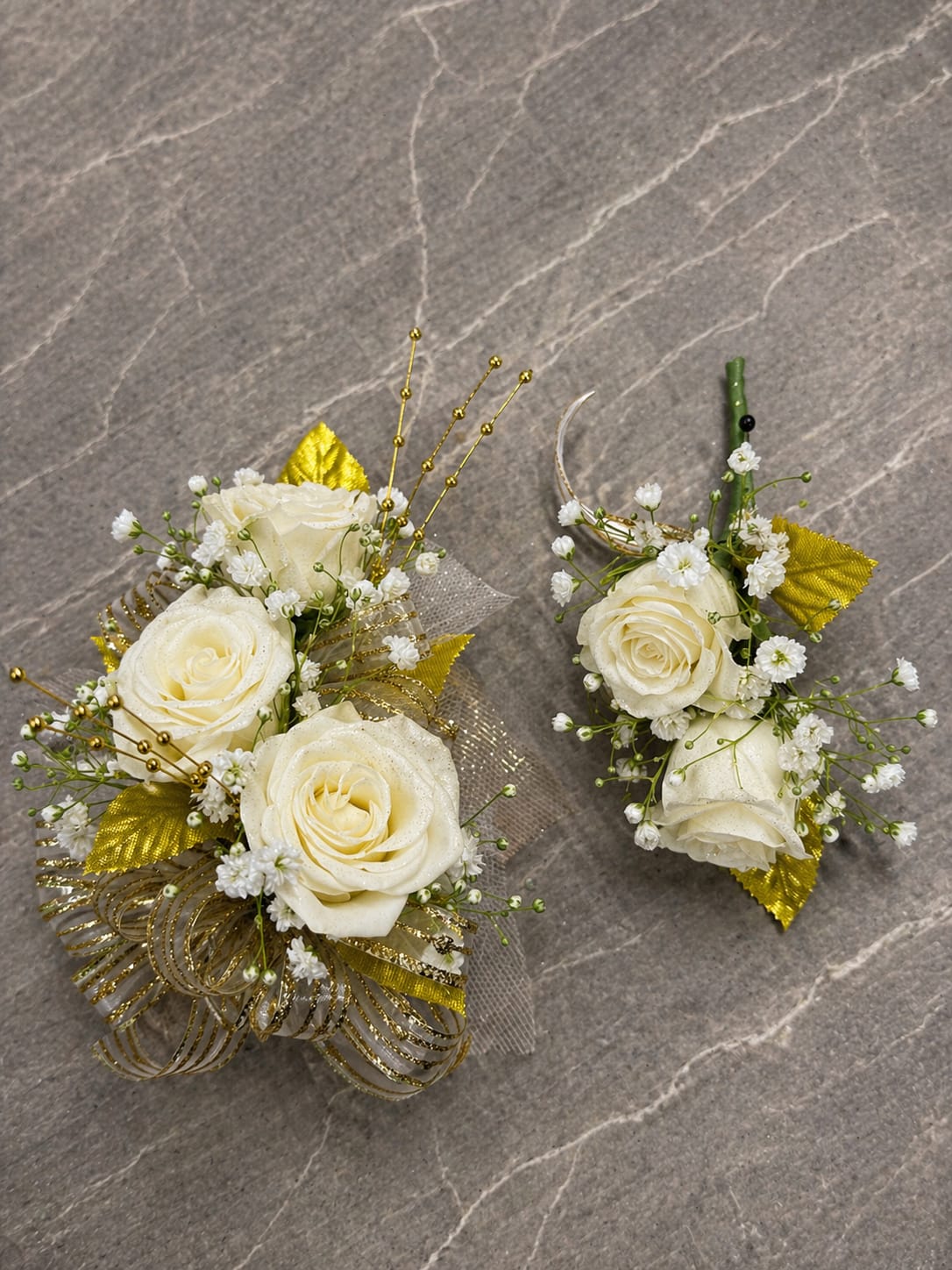 White Gold Formal Set - MAGNETIC BOUTONNIERE WARNING: CONTAINS STRONG MAGNETS. DO NOT USE IF YOU HAVE A PACEMAKER, DEFIBRILLATOR, INSULIN PUMP, COCHLEAR IMPLANT, NEUROSTIMULATOR, OR OTHER IMPLANTED MEDICAL DEVICE. KEEP AWAY FROM ELECTRONICS, CREDIT CARDS, HOTEL KEY CARDS, AND CHILDREN.  White Gold  Elegant white roses, shimmering gold accents, delicate filler flowers, and sparkling details come together in White Gold, a timeless corsage and boutonniere collection designed for prom, homecoming, dances, banquets, weddings, and formal events. The classic combination of white and gold creates a clean, sophisticated look that never goes out of style.  Standard includes a wrist corsage with 3 spray roses and a matching magnetic boutonniere with 2 roses. Deluxe includes 4 spray roses in the corsage. Premium includes 5 spray roses for additional fullness and flower coverage. All boutonnieres include 2 roses.  Perfect for prom flowers, wrist corsages, magnetic boutonnieres, corsage and boutonniere sets, homecoming flowers, dance flowers, and formal event flowers.  Because each corsage and boutonniere is individually designed, no two sets will be exactly alike. Ribbon, filler flowers, bracelets, decorative accents, and other design elements may vary based on availability. While individual details may differ, the overall color palette, roses and/or flowers, style, and appearance of the White Gold collection will be maintained.