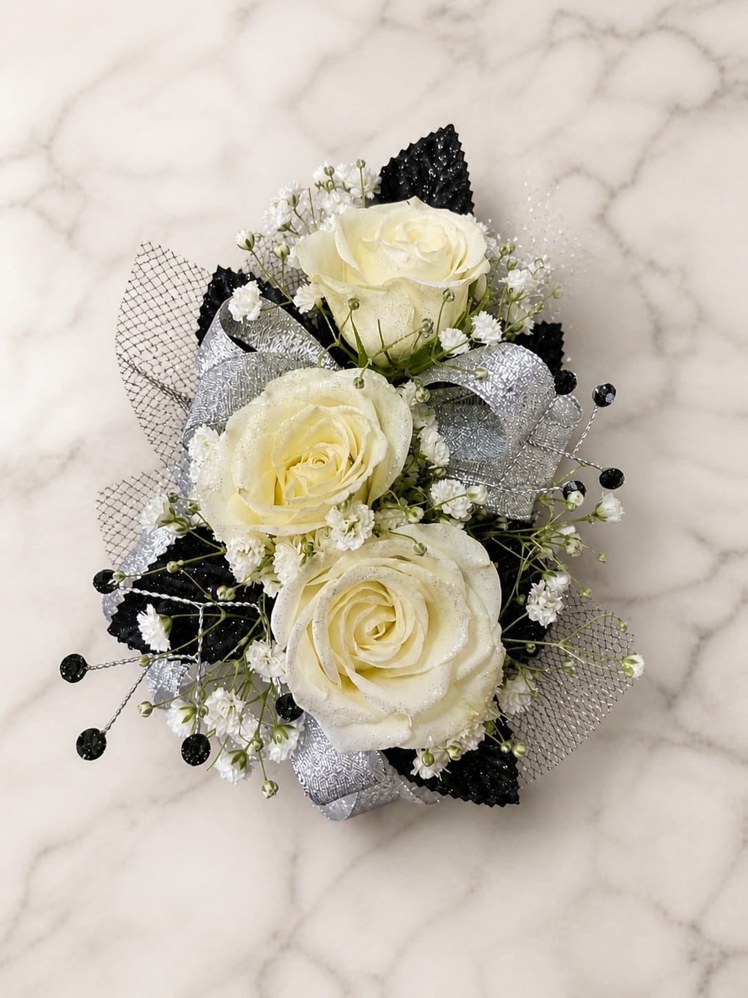 Black Tie Formal Set - MAGNETIC BOUTONNIERE WARNING: CONTAINS STRONG MAGNETS. DO NOT USE IF YOU HAVE A PACEMAKER, DEFIBRILLATOR, INSULIN PUMP, COCHLEAR IMPLANT, NEUROSTIMULATOR, OR OTHER IMPLANTED MEDICAL DEVICE. KEEP AWAY FROM ELECTRONICS, CREDIT CARDS, HOTEL KEY CARDS, AND CHILDREN.  Black Tie  White roses, black accents, silver ribbon, sparkling rhinestone details, and delicate filler flowers come together in Black Tie, a sophisticated corsage and boutonniere collection designed for prom, homecoming, dances, weddings, and formal events. Inspired by the timeless elegance of a classic tuxedo, this striking combination of black, white, and silver creates a polished look that never goes out of style.  Standard includes a wrist corsage with 3 spray roses and a matching magnetic boutonniere with 2 roses. Deluxe includes 4 spray roses in the corsage. Premium includes 5 spray roses for additional fullness and flower coverage. All boutonnieres include 2 roses.  Perfect for prom flowers, wrist corsages, magnetic boutonnieres, corsage and boutonniere sets, homecoming flowers, dance flowers, and formal event flowers.  Because each corsage and boutonniere is individually designed, no two sets will be exactly alike. Ribbon, filler flowers, bracelets, decorative accents, and other design elements may vary based on availability. While individual details may differ, the overall color palette, roses and/or flowers, style, and appearance of the Black Tie collection will be maintained.