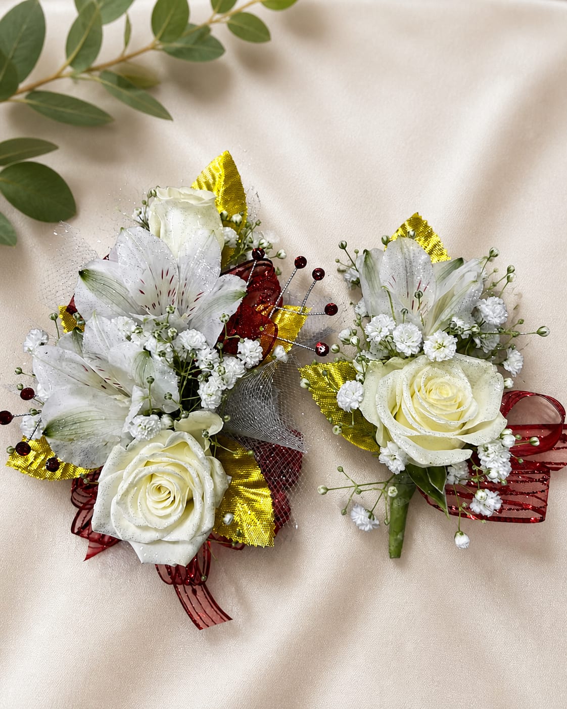 Likes &amp; Dreams Formal Set - MAGNETIC BOUTONNIERE WARNING: CONTAINS STRONG MAGNETS. DO NOT USE IF YOU HAVE A PACEMAKER, DEFIBRILLATOR, INSULIN PUMP, COCHLEAR IMPLANT, NEUROSTIMULATOR, OR OTHER IMPLANTED MEDICAL DEVICE. KEEP AWAY FROM ELECTRONICS, CREDIT CARDS, HOTEL KEY CARDS, AND CHILDREN.  Lilies &amp; Dreams  White roses, white alstroemeria lilies, red ribbon, gold accents, and delicate filler flowers come together in Lilies &amp; Dreams, an elegant corsage and boutonniere collection for prom, homecoming, dances, weddings, and formal events.  Standard includes a wrist corsage with 3 spray roses and a matching magnetic boutonniere featuring one rose and one alstroemeria lily. Deluxe includes 4 spray roses in the corsage. Premium includes 5 spray roses for additional fullness and flower coverage.  Perfect for prom flowers, wrist corsages, magnetic boutonnieres, corsage and boutonniere sets, homecoming flowers, dance flowers, and formal event flowers.  Because each corsage and boutonniere is individually designed, no two sets will be exactly alike. Ribbon, filler flowers, bracelets, decorative accents, and other design elements may vary based on availability. While individual details may differ, the overall color palette, roses and/or flowers, style, and appearance of the Lilies &amp; Dreams collection will be maintained.