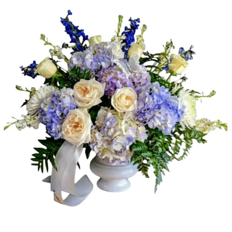 Blue and lavender floral arrangement with cream roses in a white vase