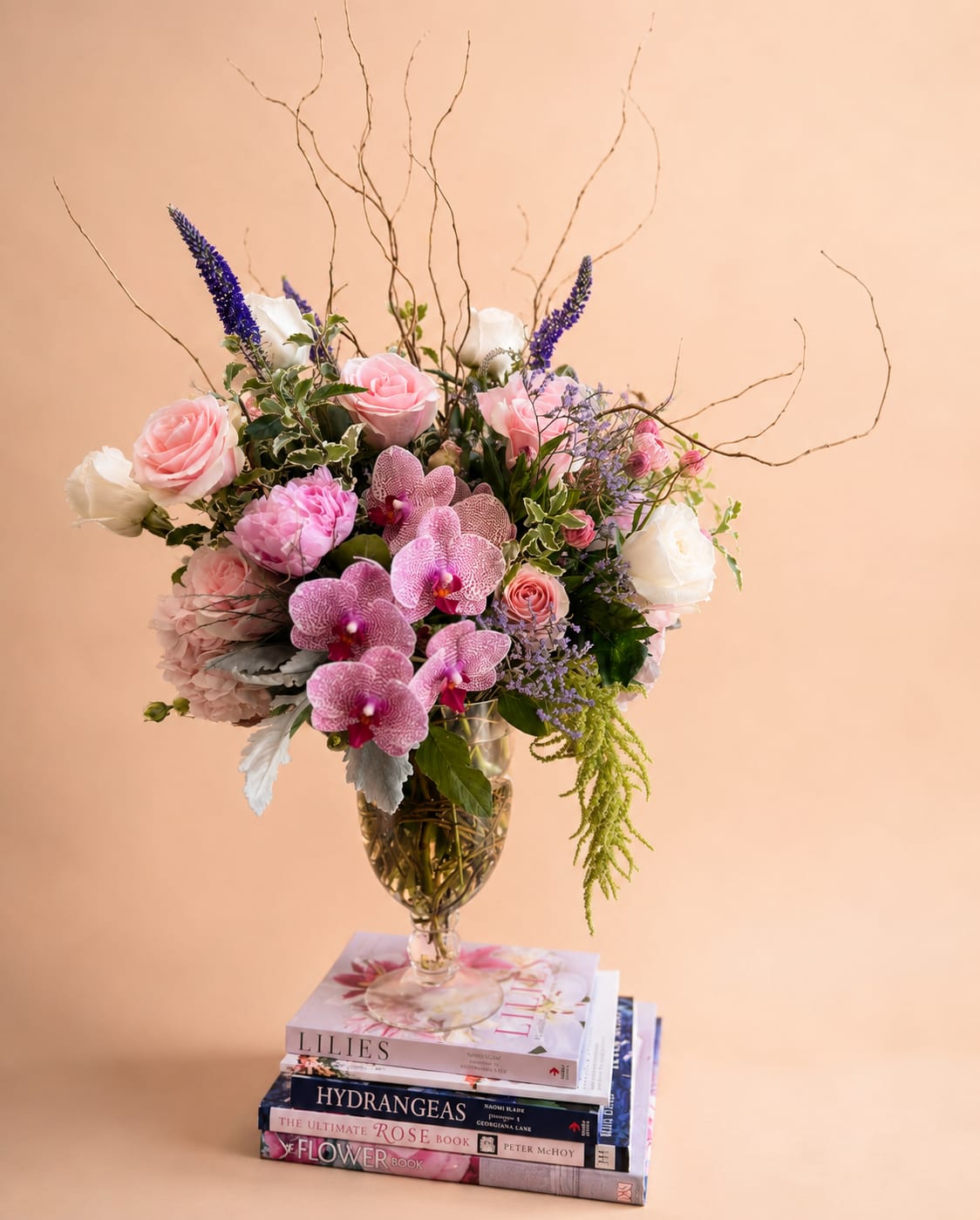 Mixed bouquet of pink roses, orchids, and white blooms in a glass vase